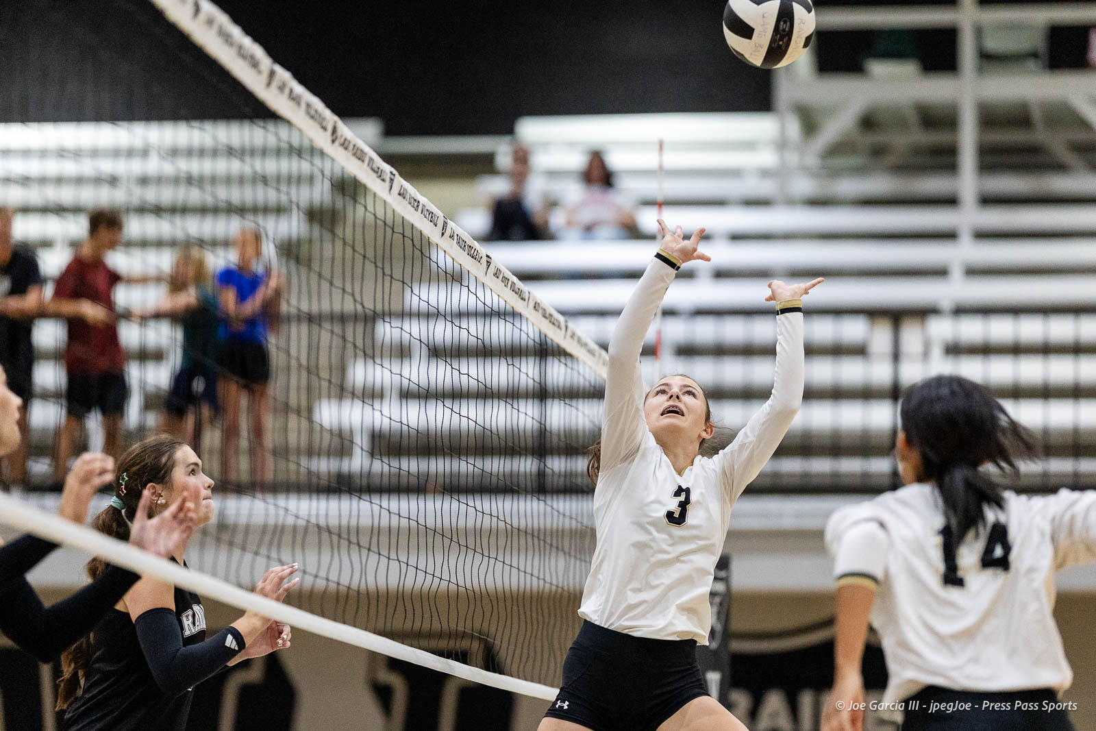 randall-showcase-2026-jpegJoe-pps-84 | Press Pass Sports Player in white jersey #3 jumps with arms raised to block a volleyball at the net as teammates watch nearby in a gym.
