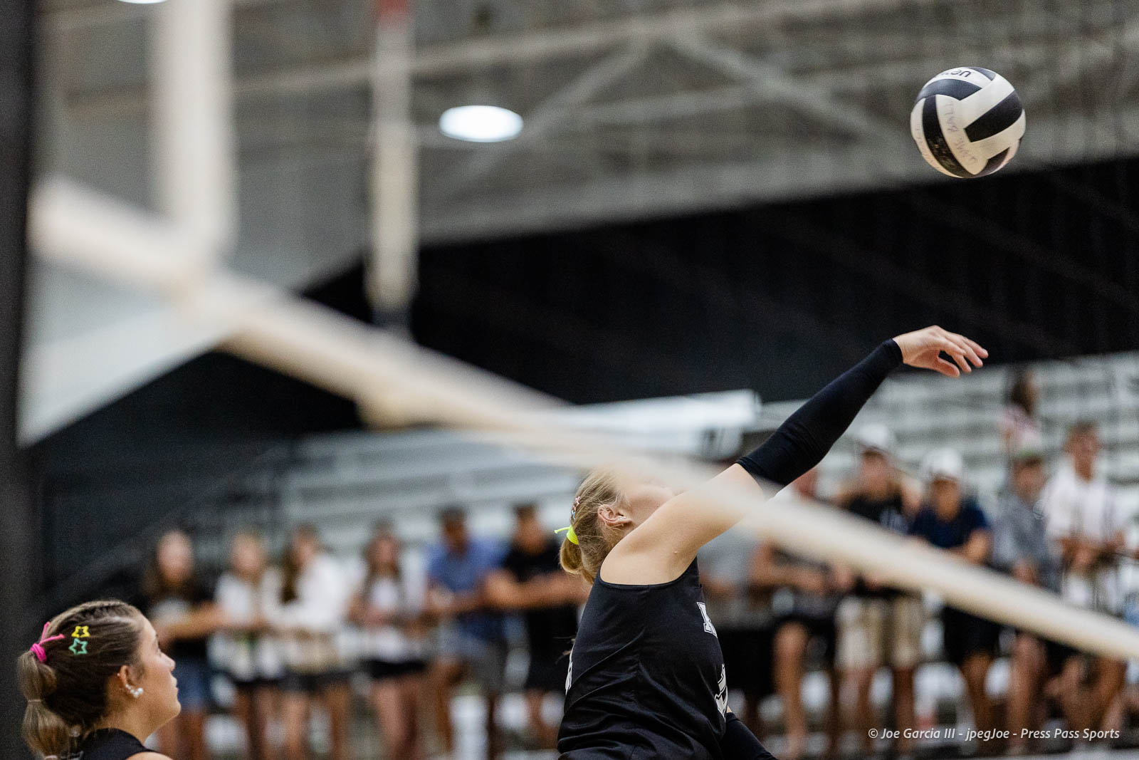 randall-showcase-2026-jpegJoe-pps-90 | Press Pass Sports Female volleyball player in black uniform spikes ball above net in an indoor gym with crowd on bleachers watching.