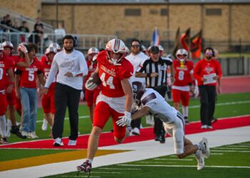image6 7 | Press Pass Sports Red-team football player (No. 44) in a sprint with the ball, pursued by a defender on a green artificial turf field as teammates and crowd look on.