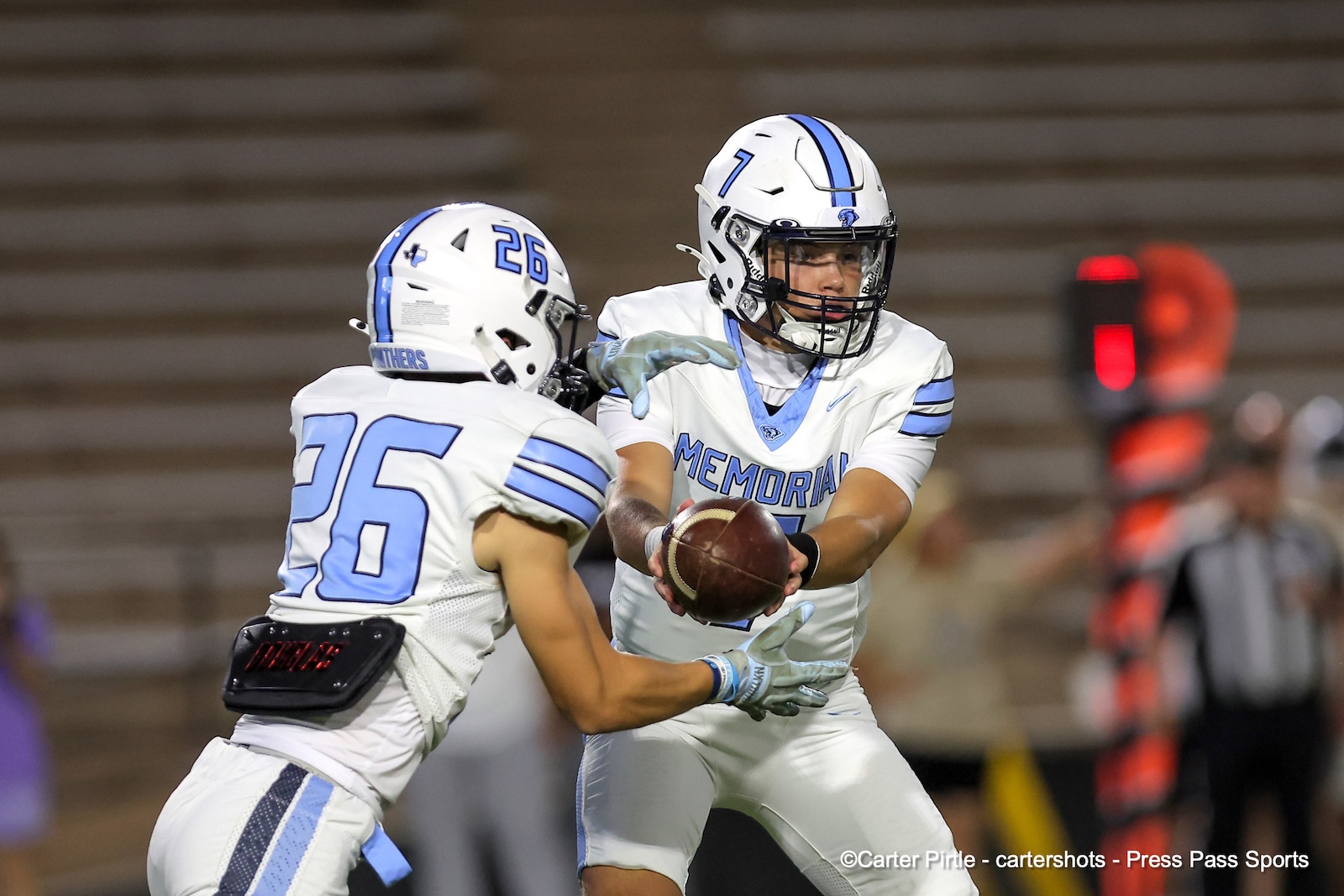 Memorial football players in white and blue, one with the ball preparing a handoff as another approaches in a game.
