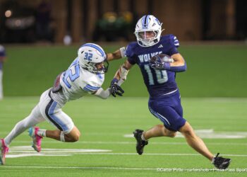 20260903-Memorial-WestPlains-FB-008 | Press Pass Sports Two football players collide on a green turf field at night: white #32 reaching for the ball carrier in blue #10 holding the ball clutched to his chest