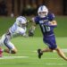 20260903-Memorial-WestPlains-FB-008 | Press Pass Sports Two football players collide on a green turf field at night: white #32 reaching for the ball carrier in blue #10 holding the ball clutched to his chest