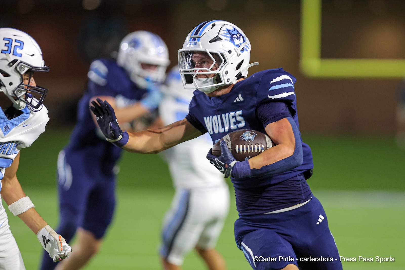 Football player in blue Wolves uniform runs with the ball, pursued by a defender in white on a green field.