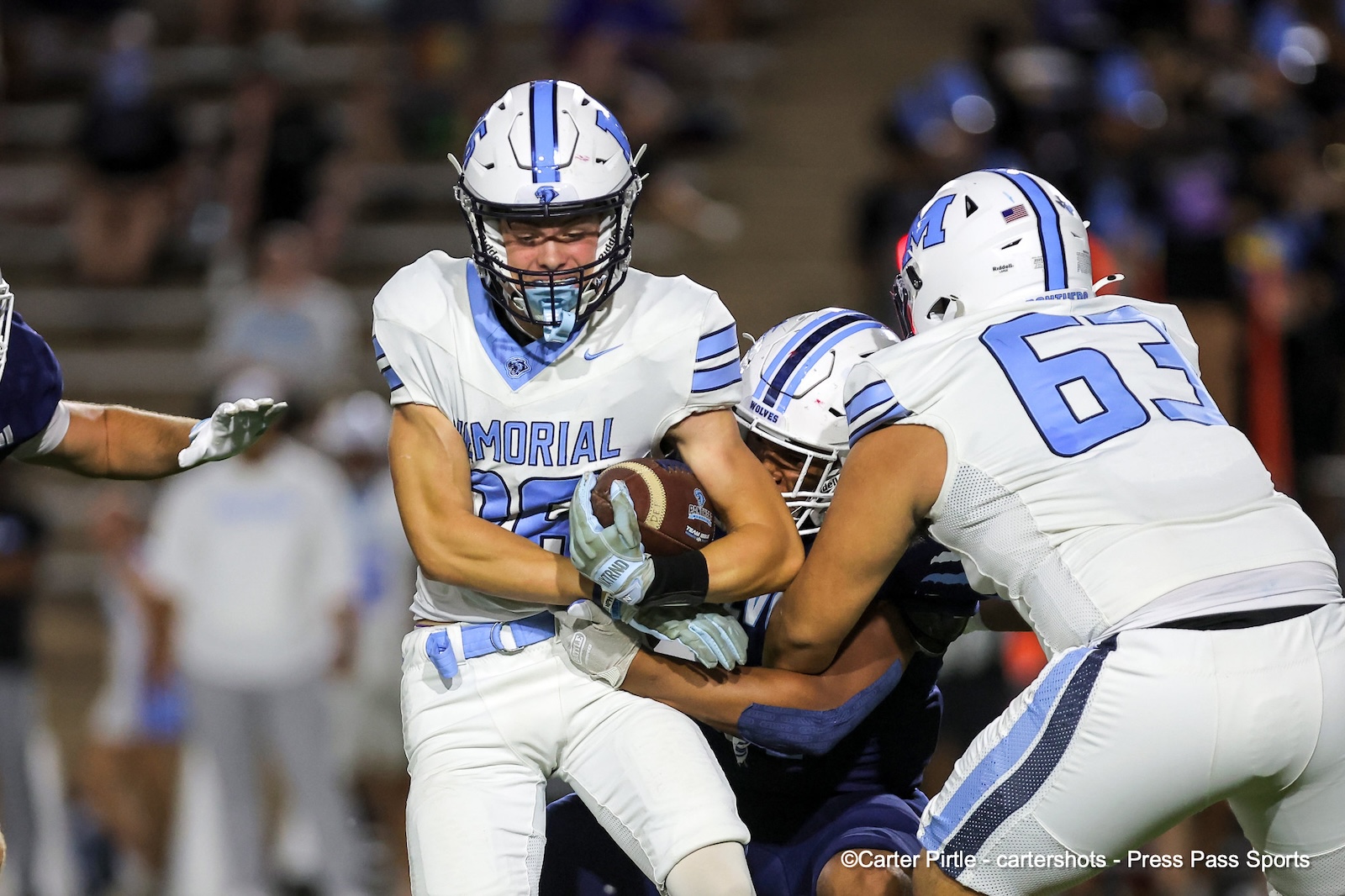 Memorial football player with the ball tackled by opponents during a nighttime game.