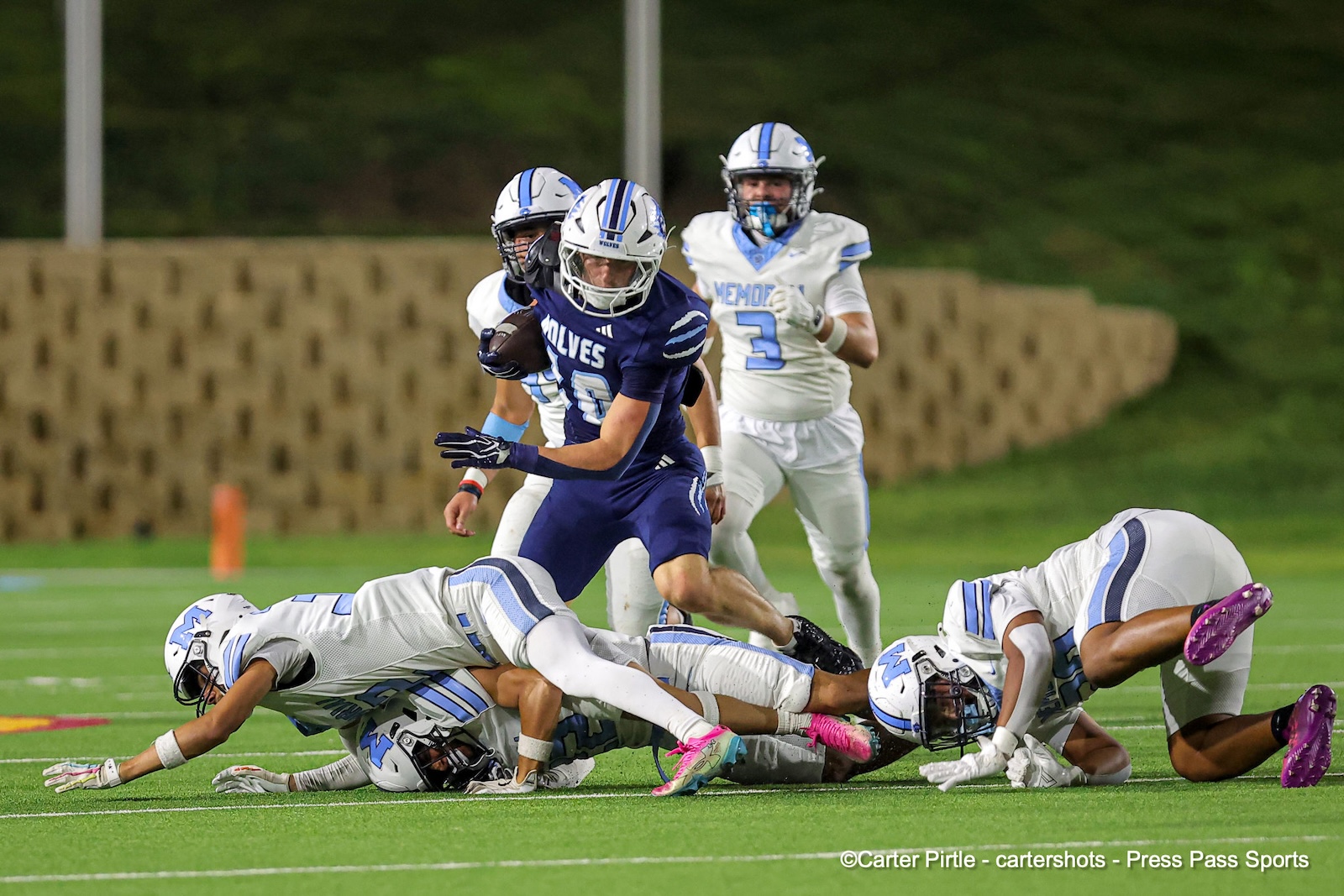Purple Wolves ball carrier evades white-uniformed defenders during a tackle on a bright football field.