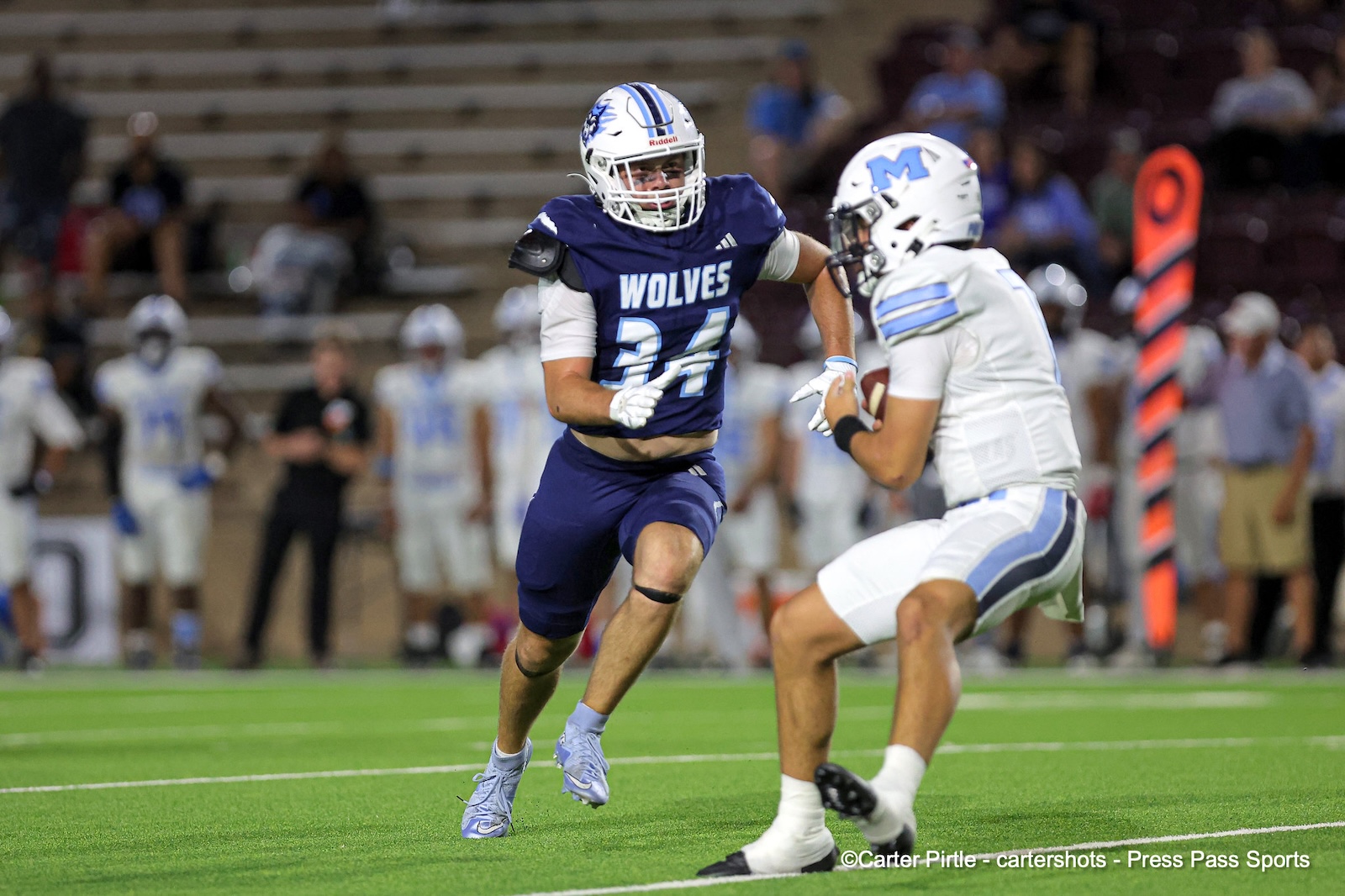Wolves defender in blue #24 charges toward a white-jersey opponent during a football game on a green field.