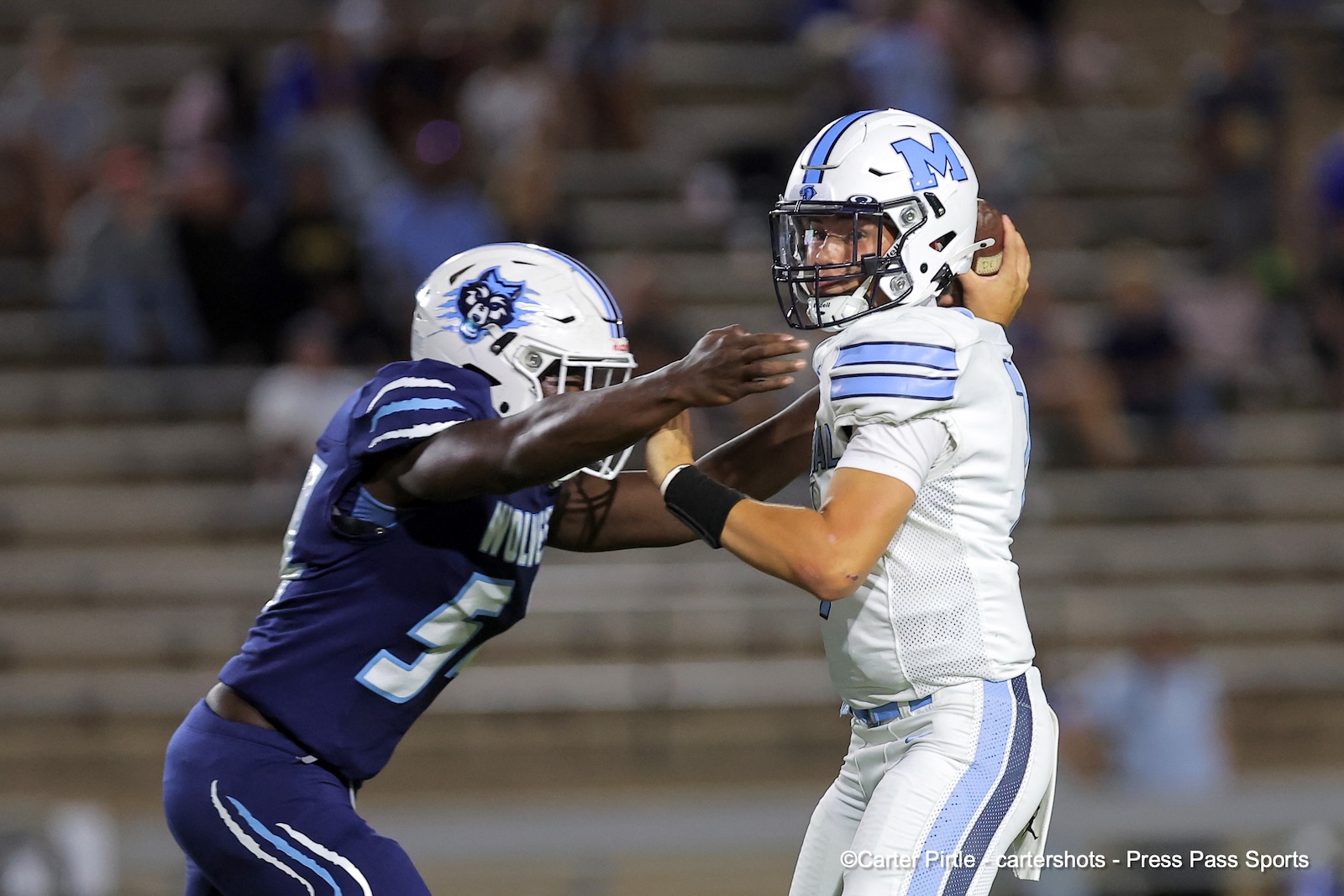 Two football players collide on the field during a game, one in white/blue and the other in purple, reaching for each other.