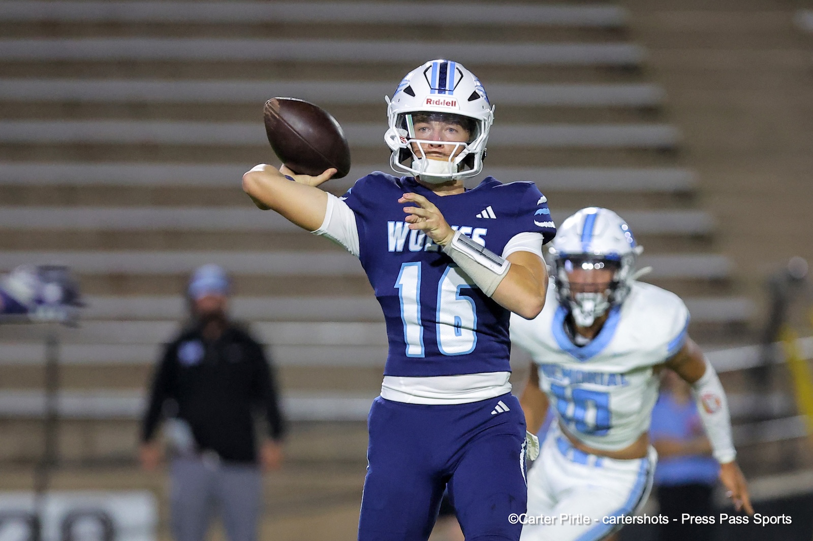Quarterback in a blue Wolves jersey (#16) throws a pass, football in midair, with a pursuing defender in white in the background.