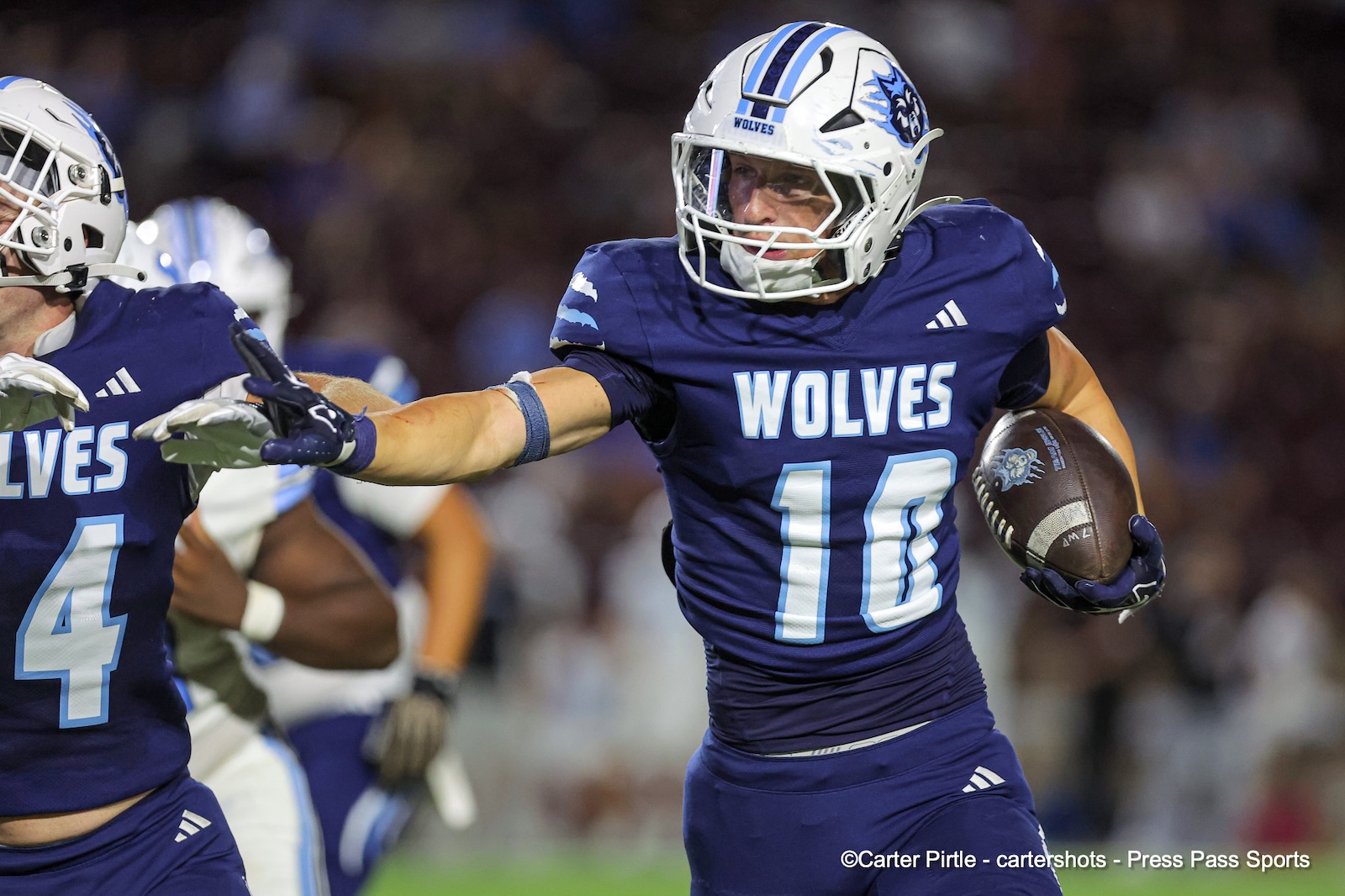 Wolves football player wearing #10 runs with the ball during a game, reaching forward for a gain.