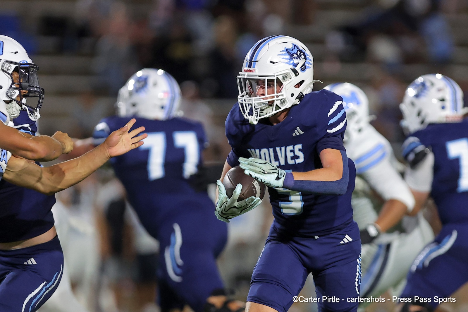A football player in a blue Wolves uniform runs with the ball, looking for space while defenders close in.
