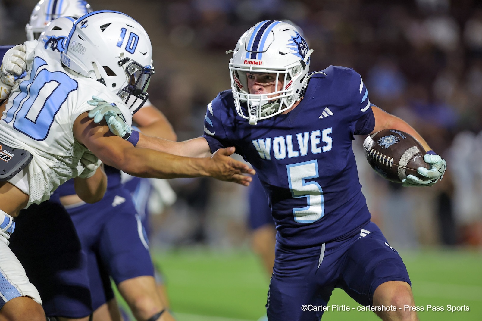 Wolves football player in navy jersey #5 guards the ball while rushing forward, pursued by a defender in white.