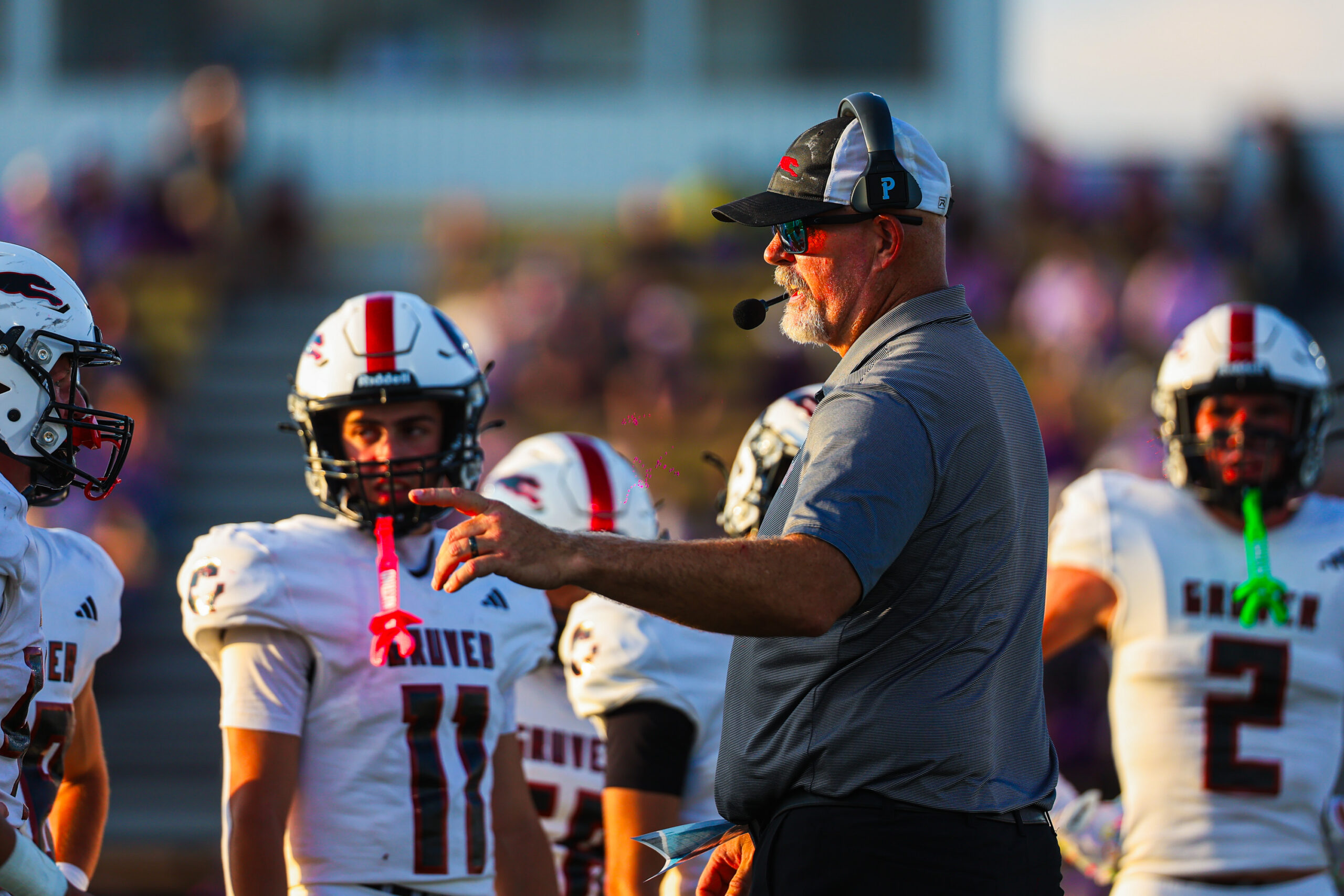 MAIRYN-04 | Press Pass Sports Football coach with headset lecturing a huddle of players in white uniforms on the field.