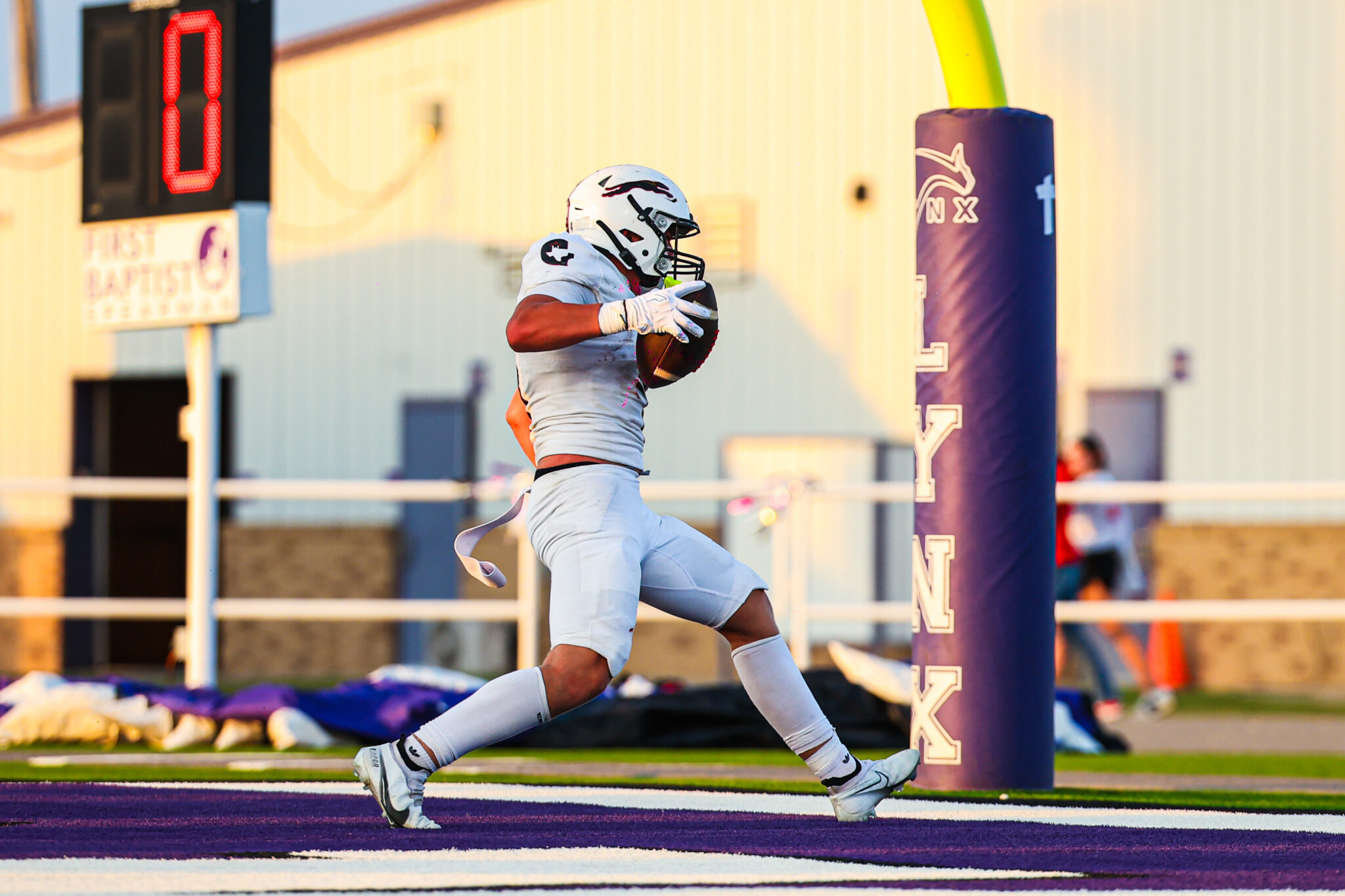 MAIRYN-07 | Press Pass Sports Football player in white uniform running with the ball toward the end zone on a purple field, goal post in background
