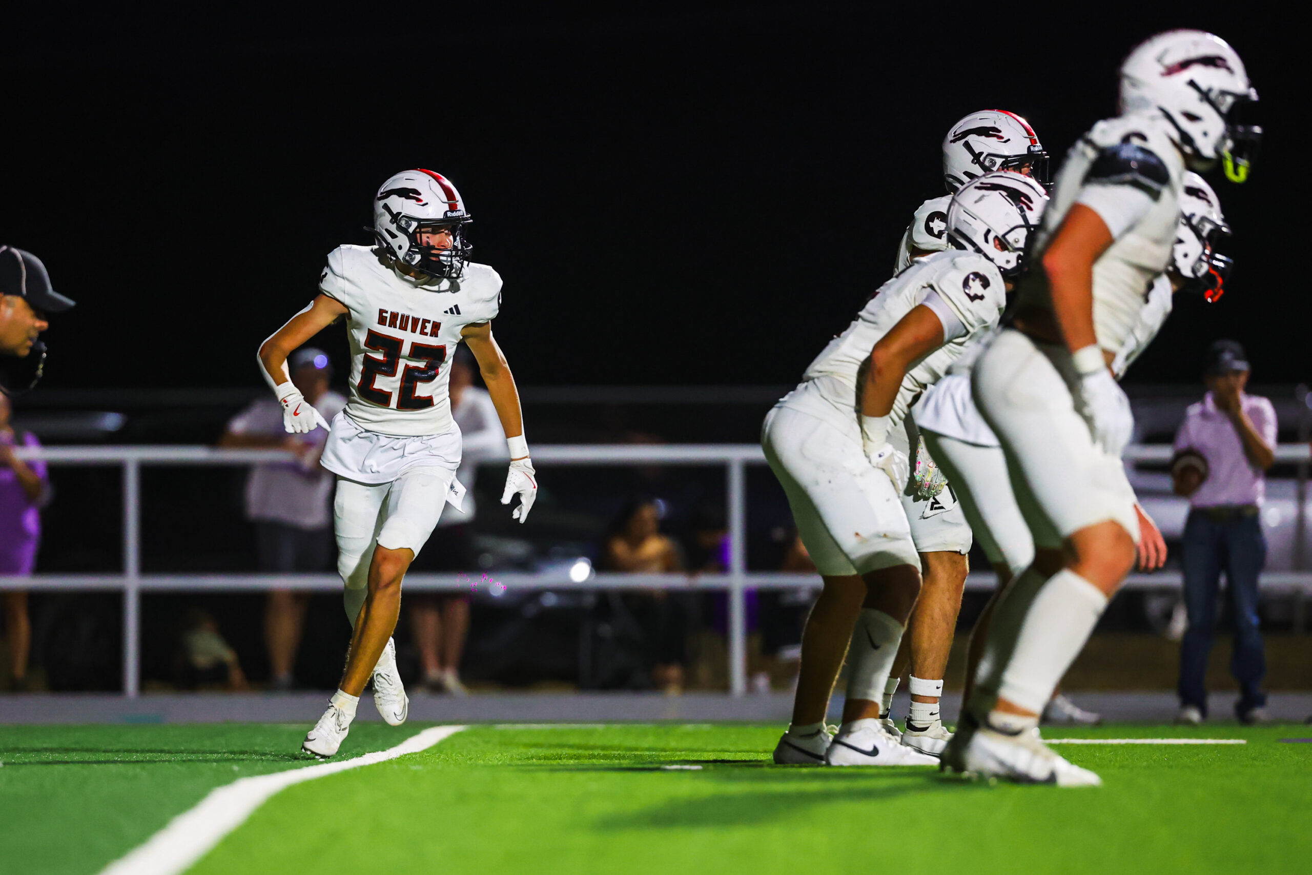 MAIRYN-12 | Press Pass Sports Football players in white jerseys on a green field at night; number 22 player (GROVER) runs forward while teammates line up behind him on the sideline.