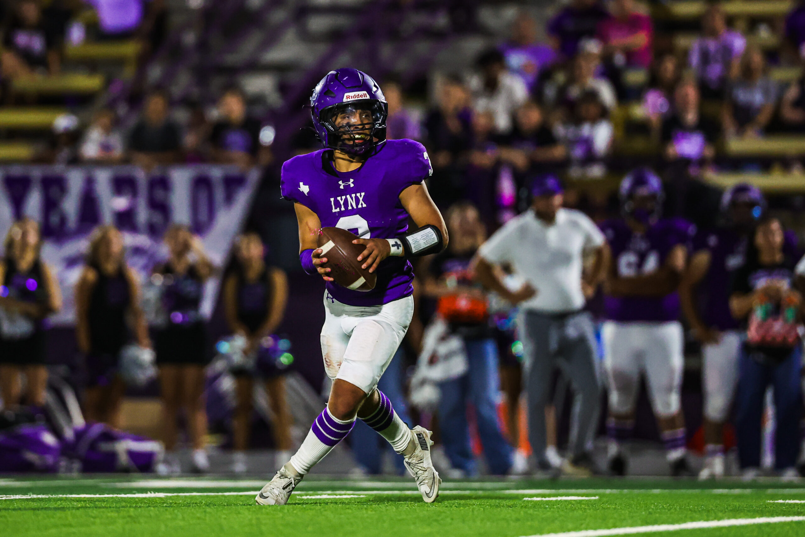 MAIRYN-16 | Press Pass Sports A football player in a purple Lynx uniform runs with the ball on a green field, crowd cheering in purple in the stands behind him (night game).