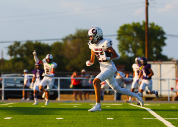 MAIRYN-18 | Press Pass Sports Football player in a white uniform carrying a football and sprinting down the field during a game on a green turf.