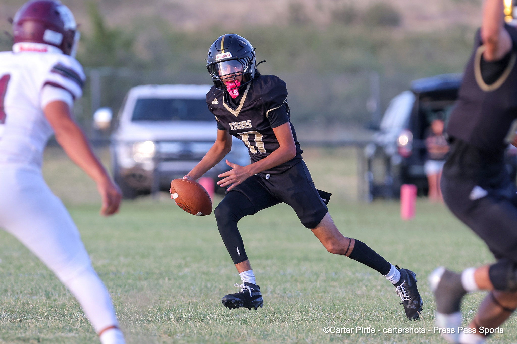 Player in black uniform with gold trim runs with the football during a game on a grassy field, defenders approaching.