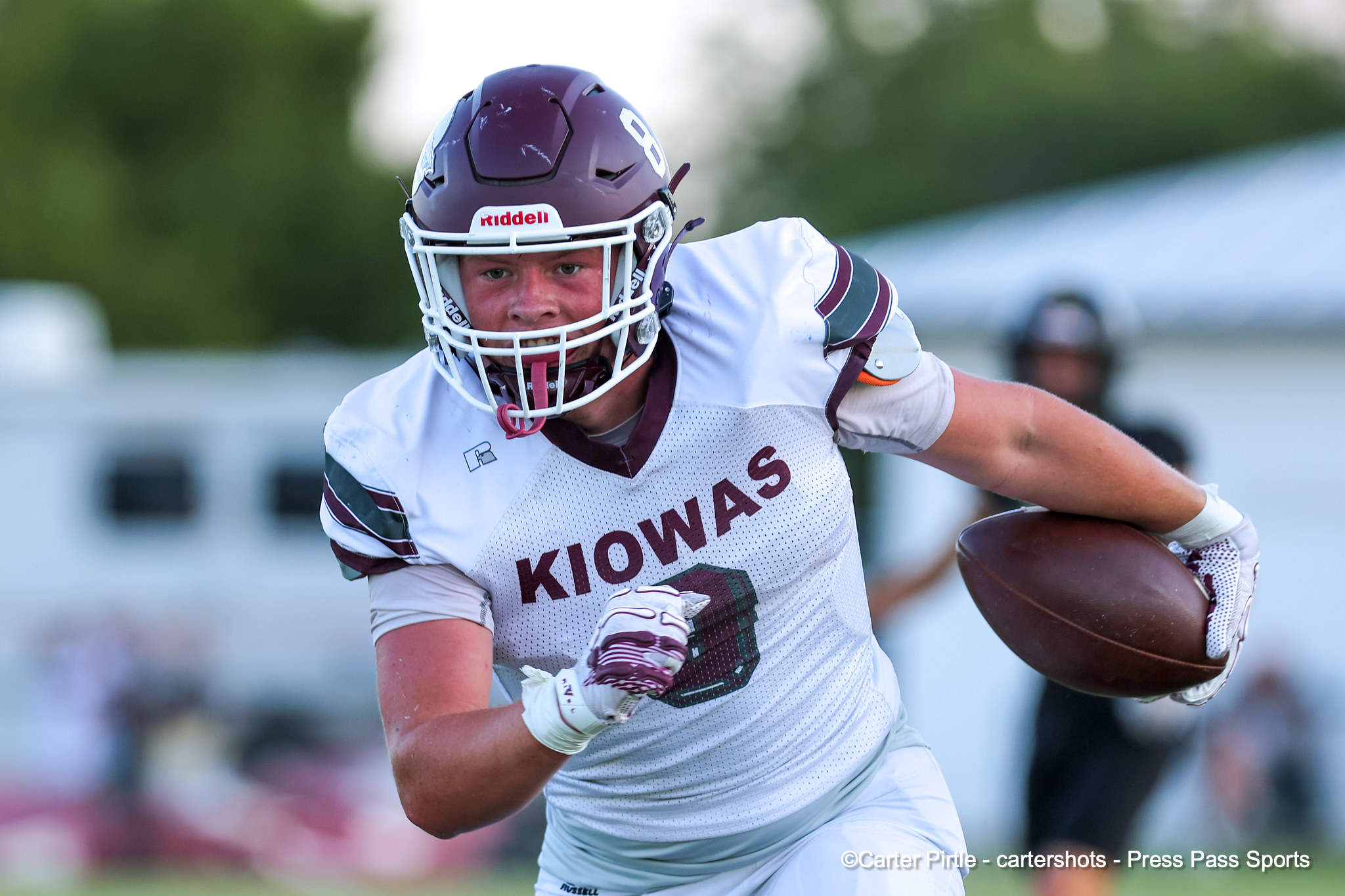 Football player in a white Iowa jersey runs with the ball, wearing a maroon helmet and white facemask.