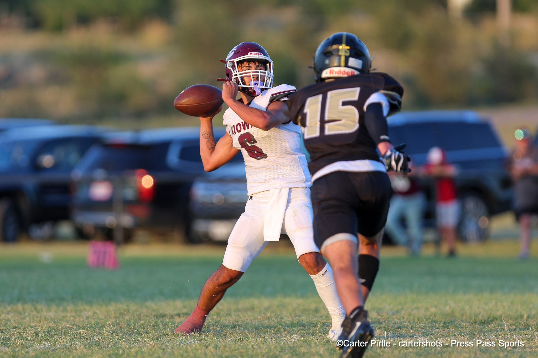 Football player in white jersey throws a pass while a defender in black jersey (#15) closes in on a grassy field.
