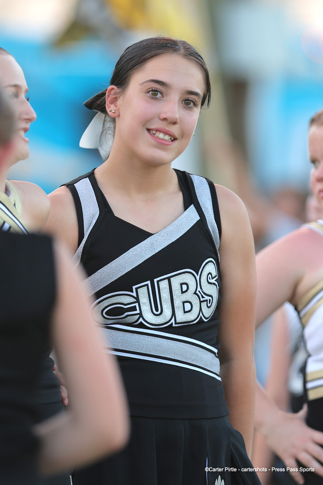 Young cheerleader in a black and silver uniform with'CUBS' lettering, smiling at a crowd.