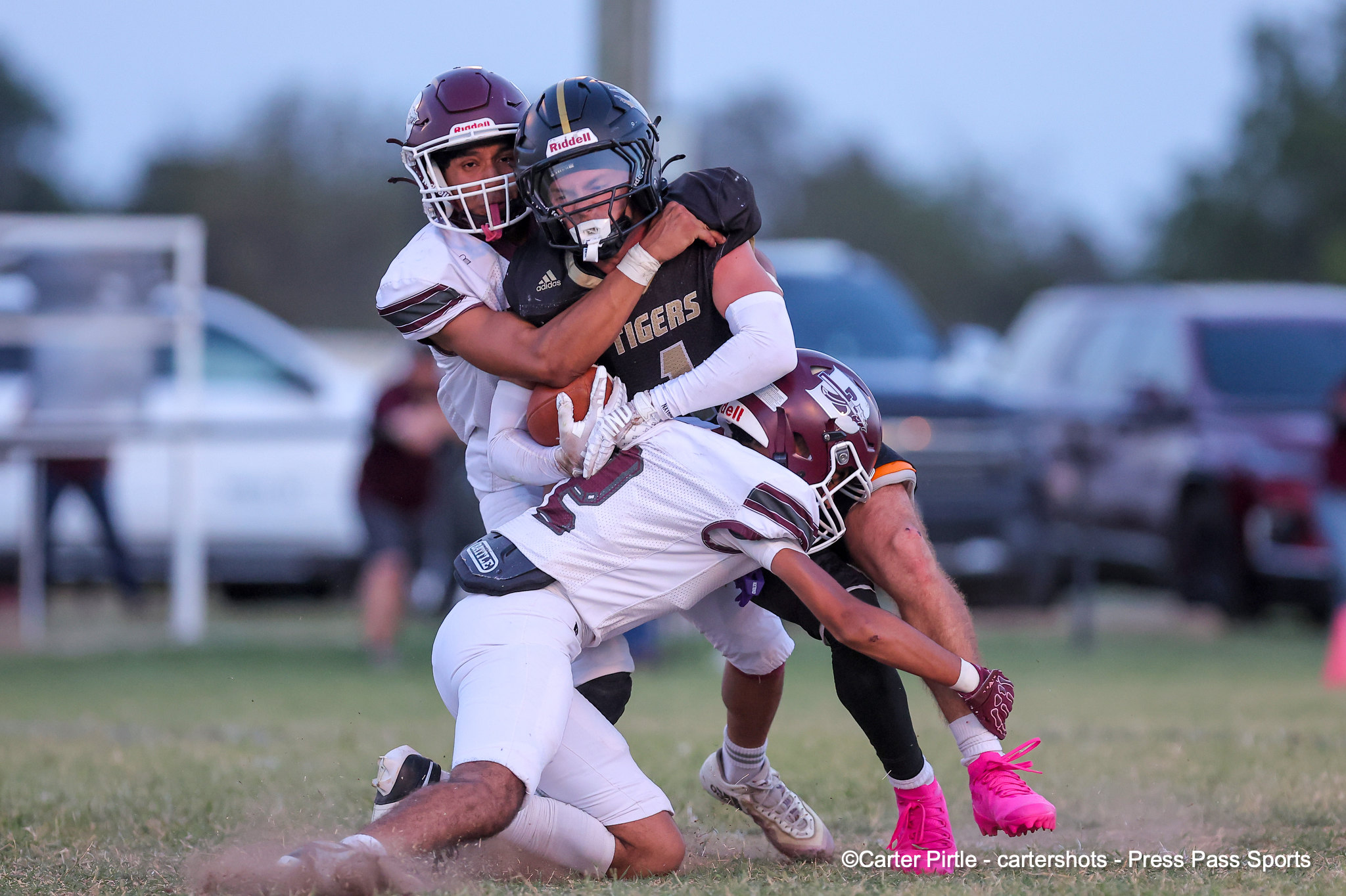 Two football players in a tackle: one in a white uniform grabs the other in a dark uniform during a game on a grassy field.