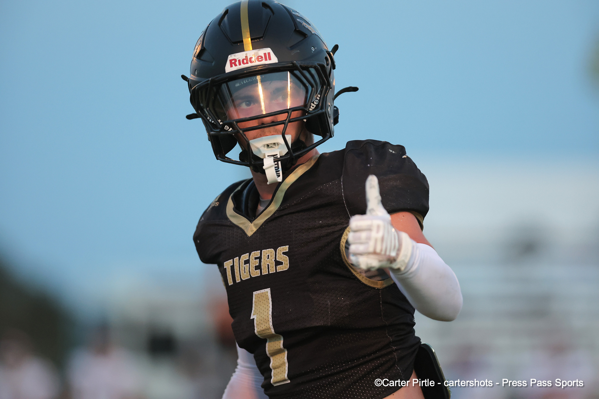 American football player in a black and gold Tigers uniform and helmet, pointing toward the camera on a blurred stadium field behind him.