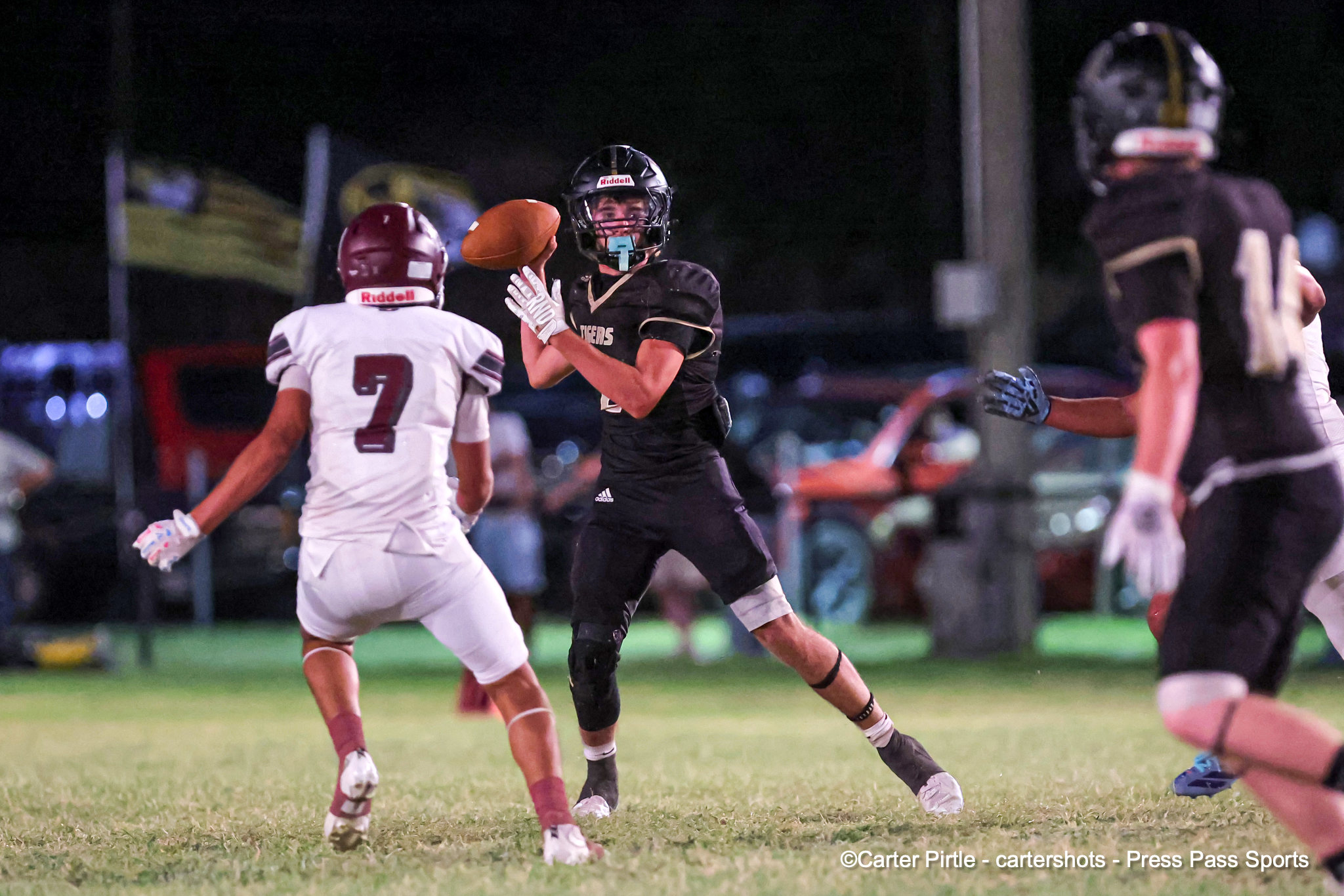 Nighttime football action: quarterback in black uniform about to throw the ball while a defender in white closes in.