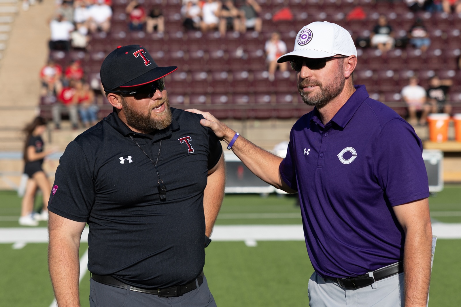 THS-CHS-FB-1 | Press Pass Sports Two coaches on a football field, one in a black polo with a Texas Tech logo, the other in a purple polo with a white cap, arm around each other.