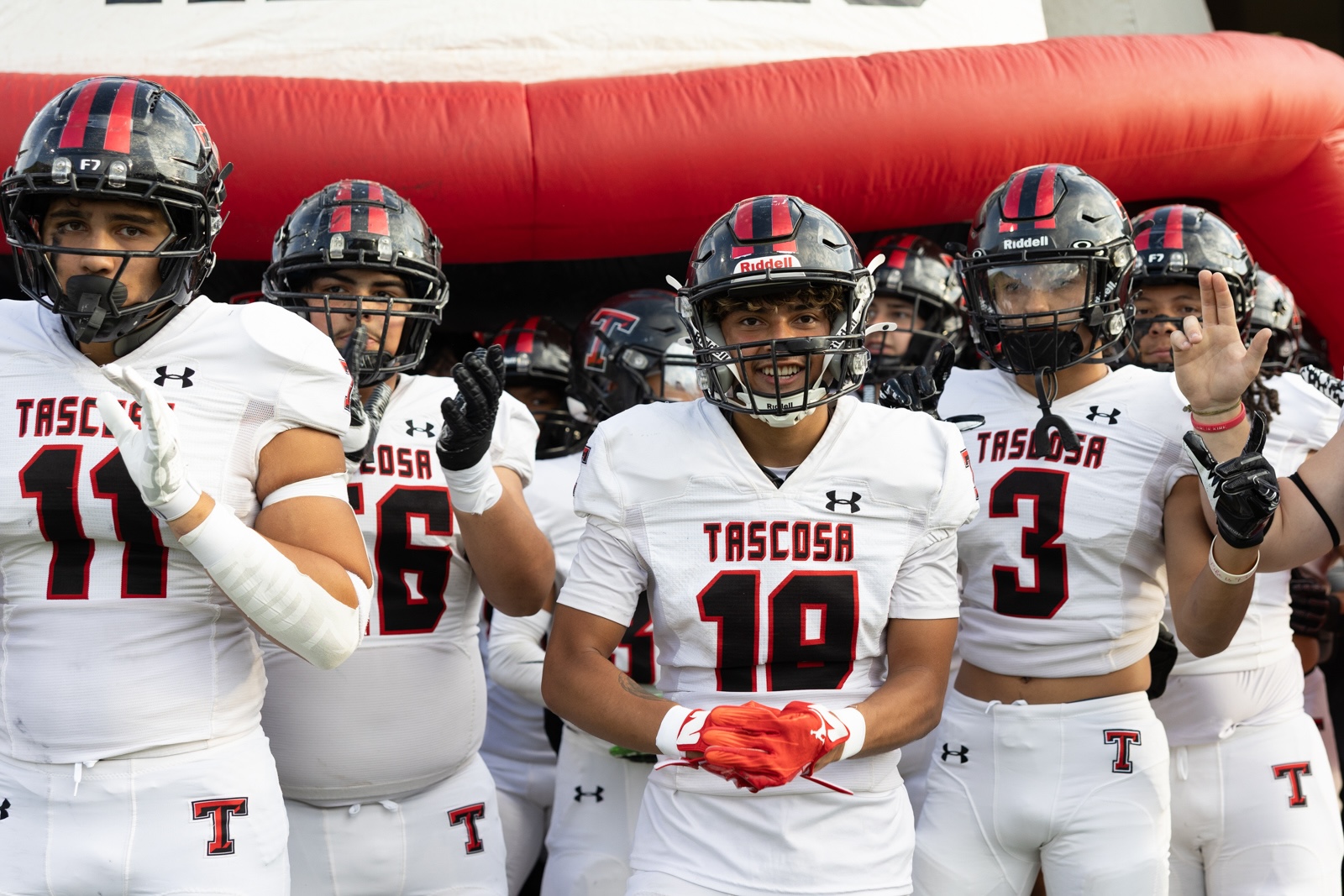 THS-CHS-FB-2 | Press Pass Sports Tascosa High School football players in white uniforms and red helmets walk through a red inflatable tunnel before a game, led by #18 center.