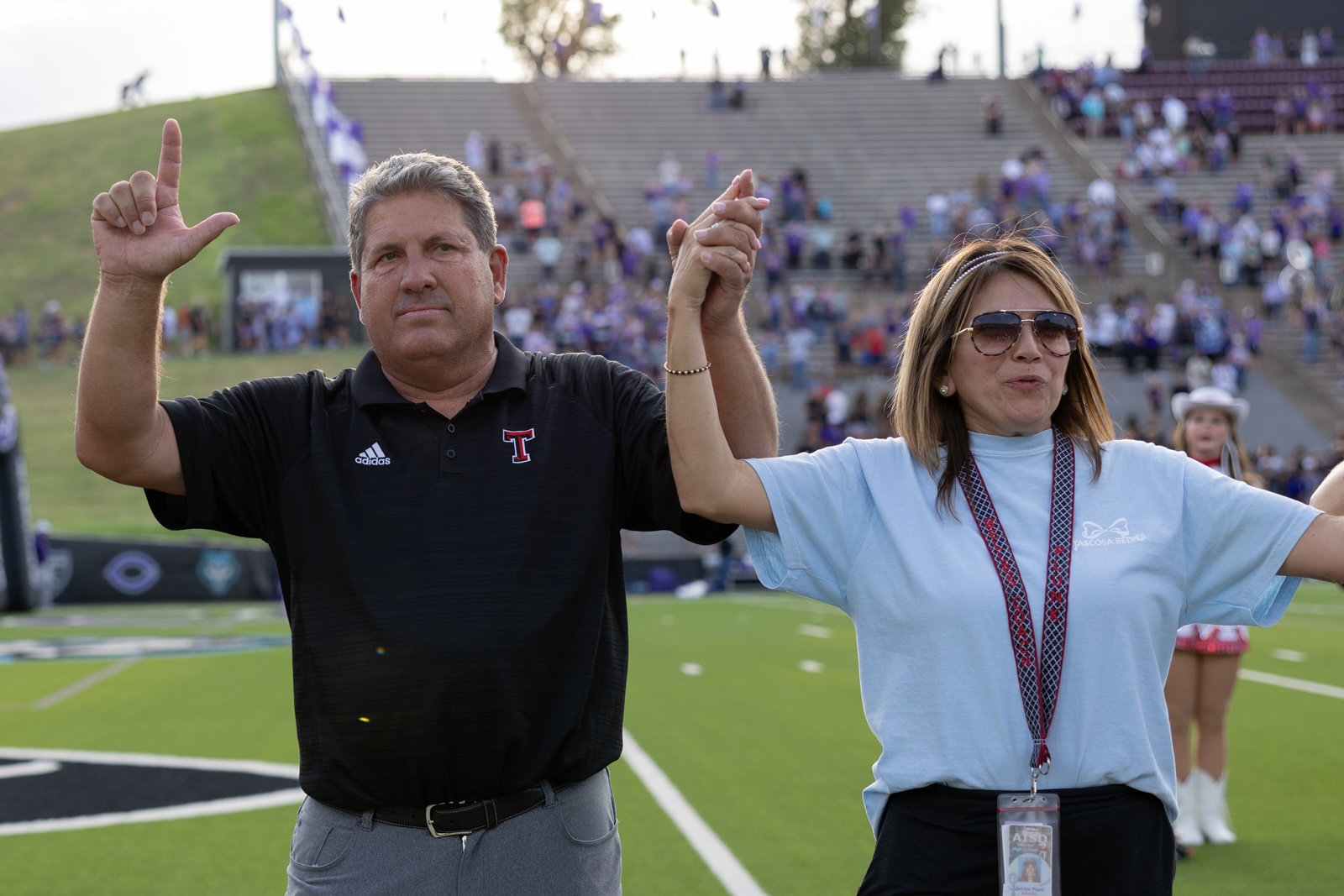 THS-CHS-FB-3 | Press Pass Sports Two adults stand on a football field, raising their clasped hands in victory as the crowd cheers in the stands behind them.
