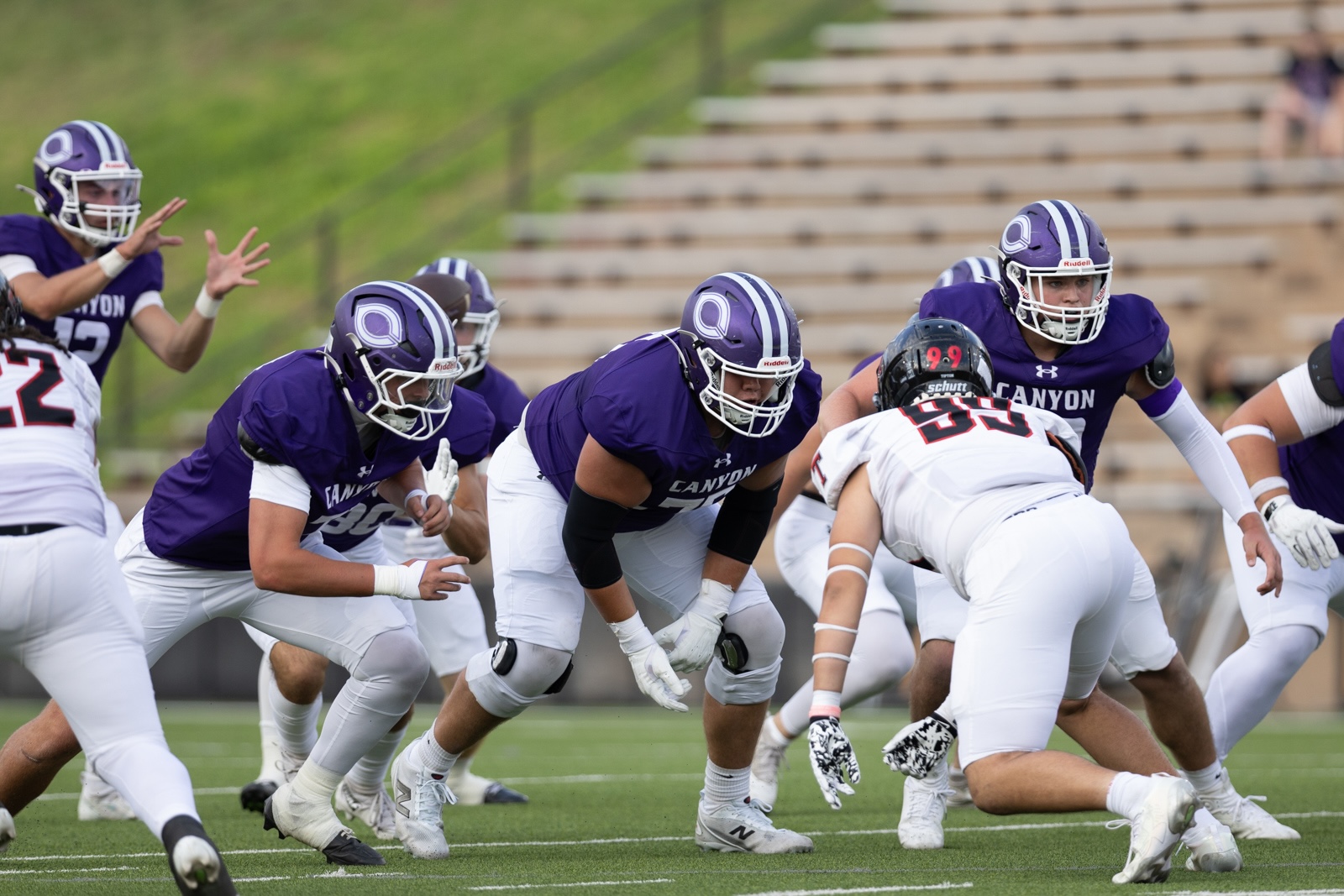 THS-CHS-FB-6 | Press Pass Sports Canyon football players in purple uniforms clash at the line of scrimmage during a play on a green field.