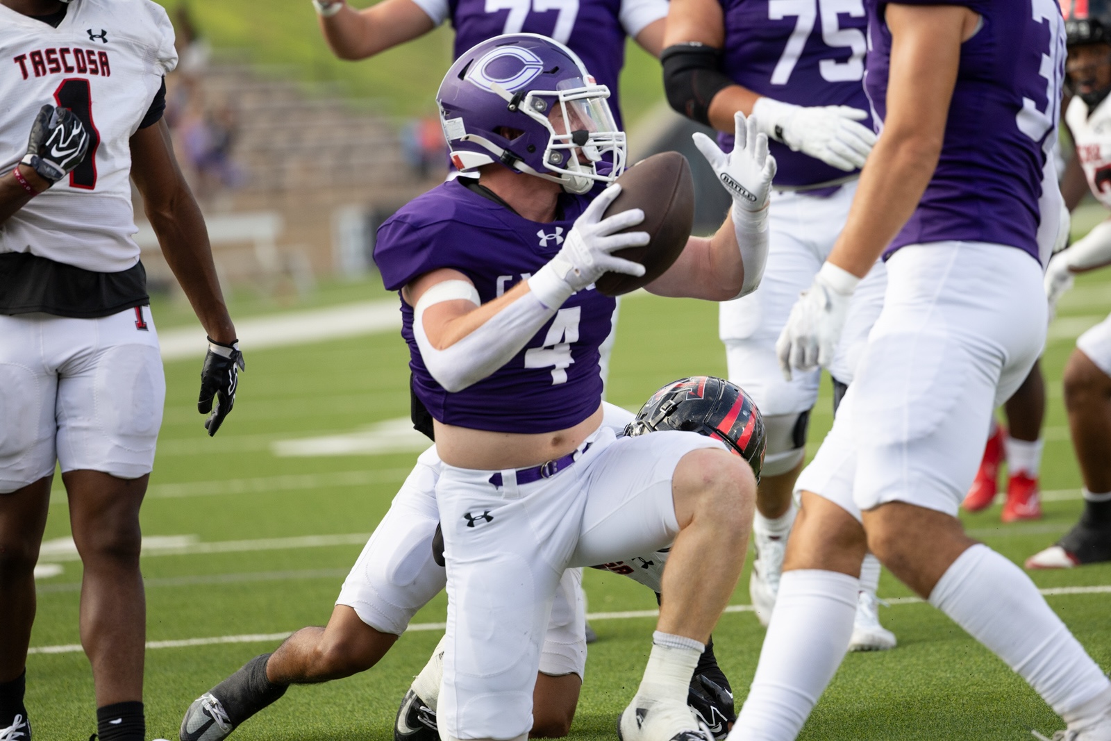 THS-CHS-FB-10 | Press Pass Sports A purple-clad football player (number 4) catches a ball while being tackled by a defender in white, on a green turf field.