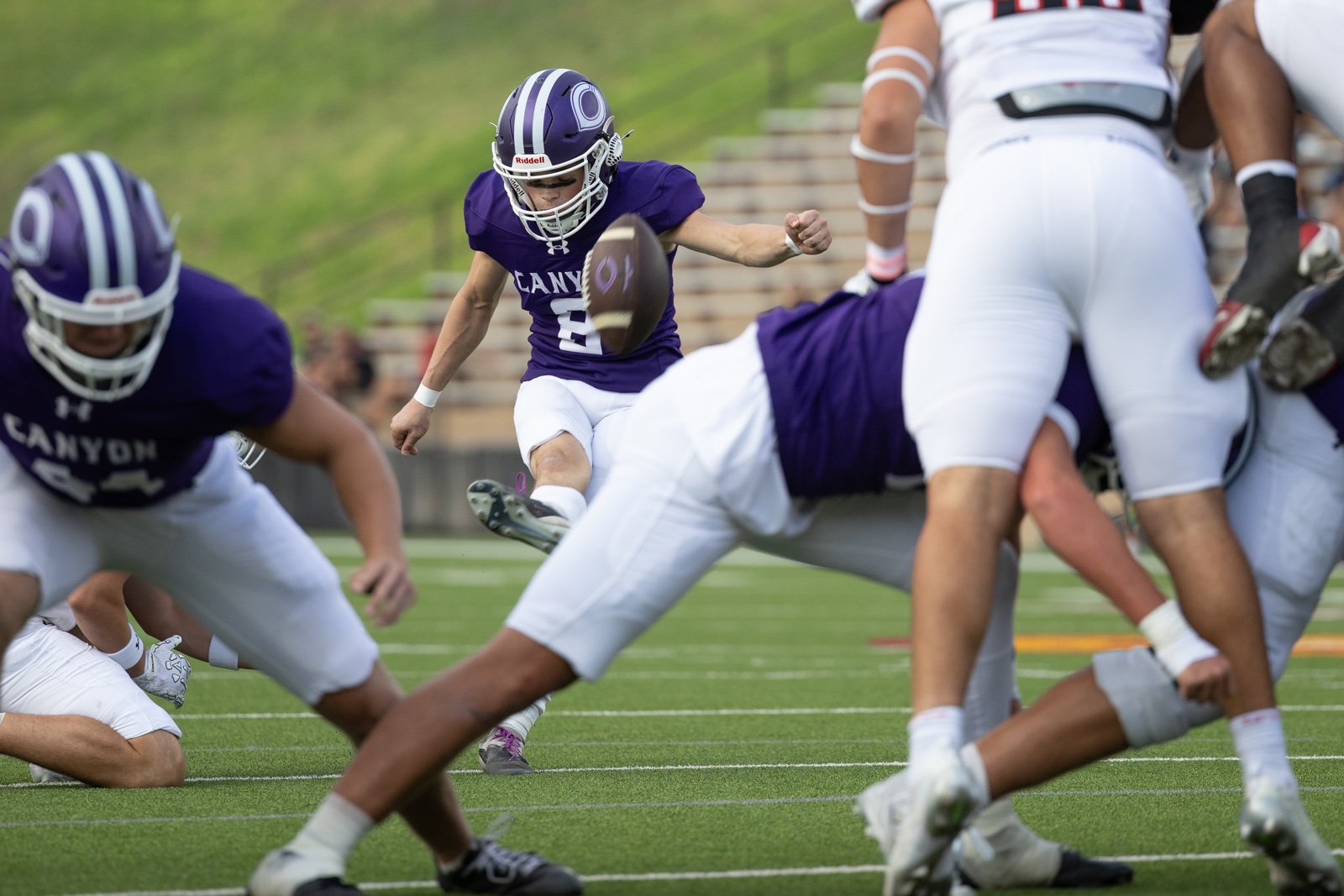 THS-CHS-FB-12 | Press Pass Sports A football player in a purple jersey kicks the ball while teammates block nearby on a green field.