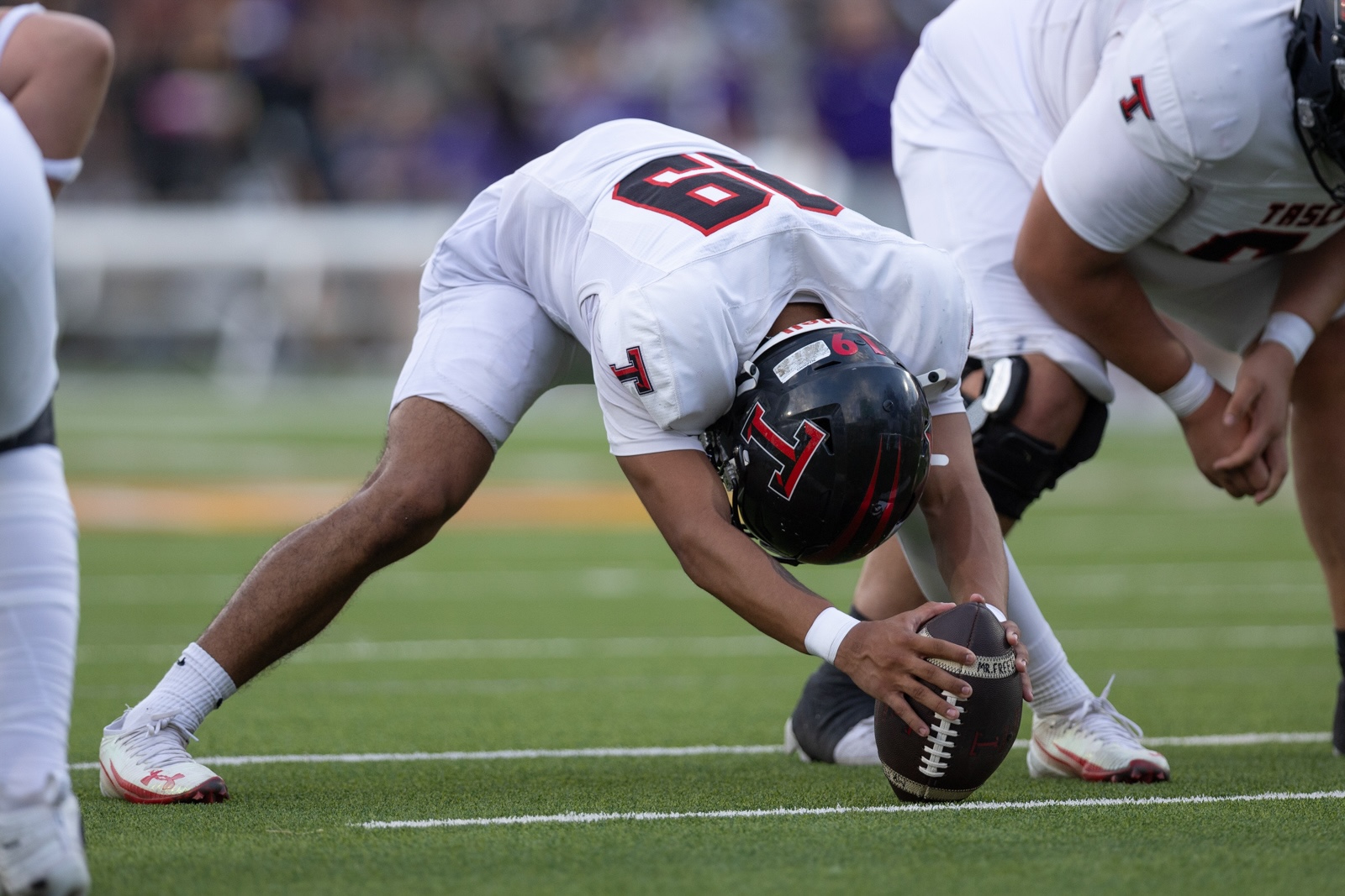 THS-CHS-FB-15 | Press Pass Sports Football player in a white uniform bends over to set the ball on the turf for a snap.