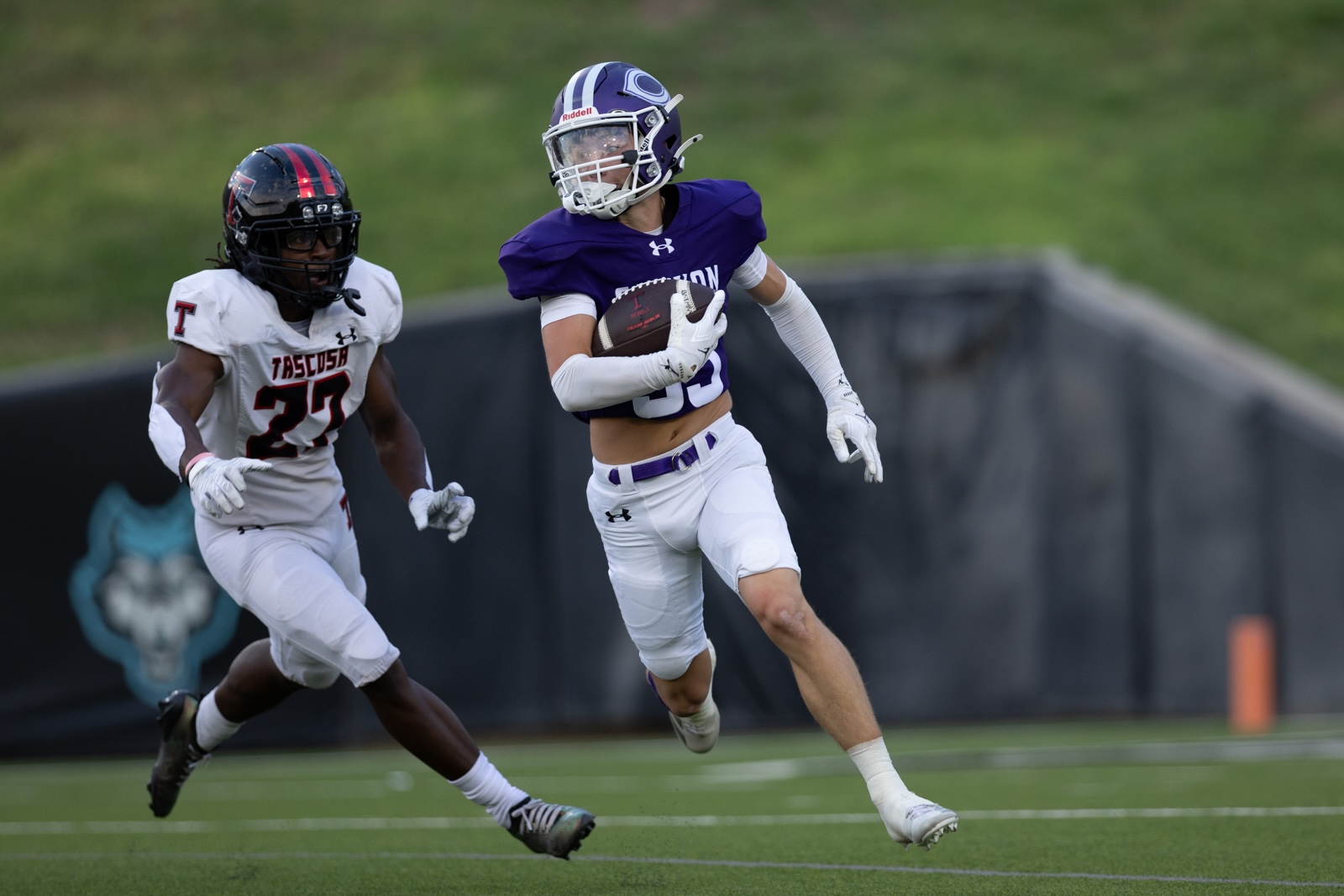 THS-CHS-FB-18 | Press Pass Sports Purple-jersey running back carries the football as a white-jersey defender pursues on a green turf football field.