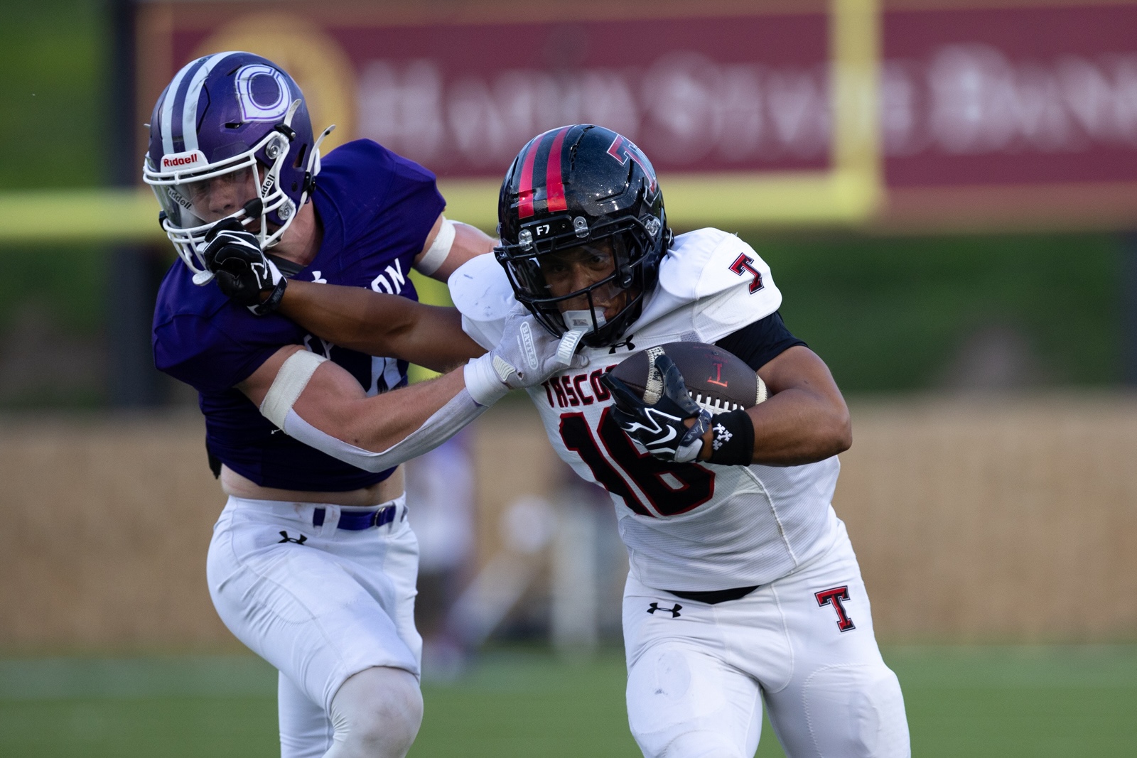 THS-CHS-FB-20 | Press Pass Sports Two football players collide: a white-uniform runner with the ball is tackled by a purple-uniform defender on a grass field.