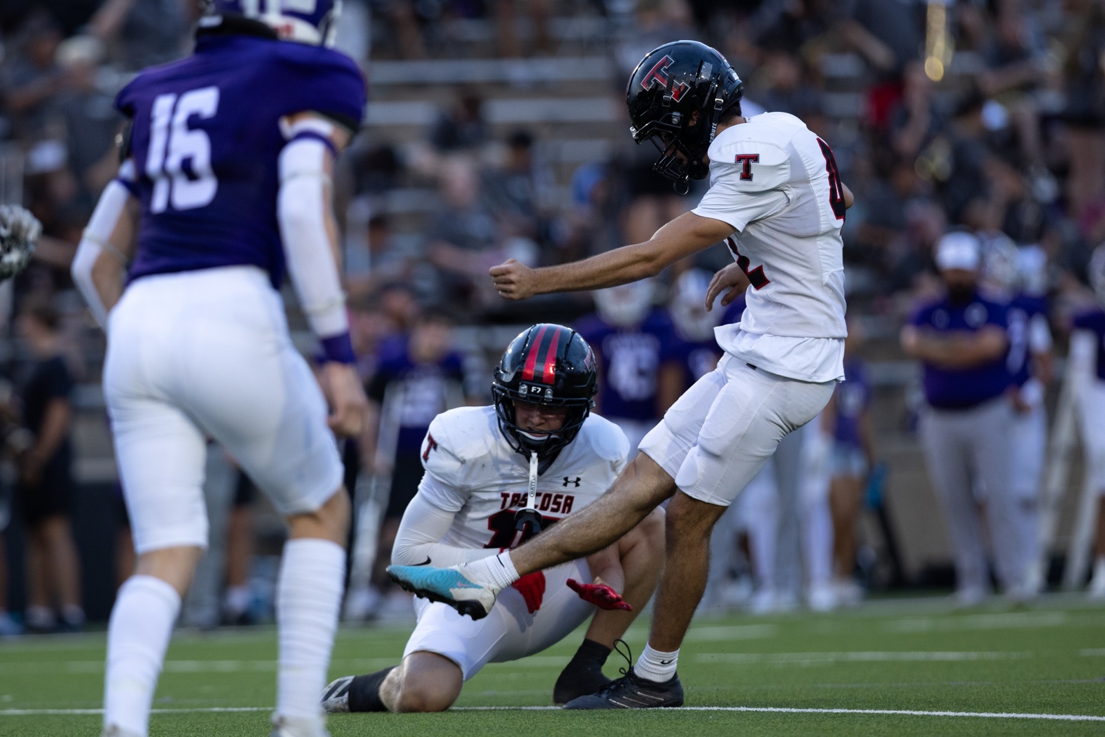 THS-CHS-FB-22 | Press Pass Sports College football scene: a player in a white jersey leaps while another white-jersey player falls to the turf, with a purple-uniform defender nearby on the field.