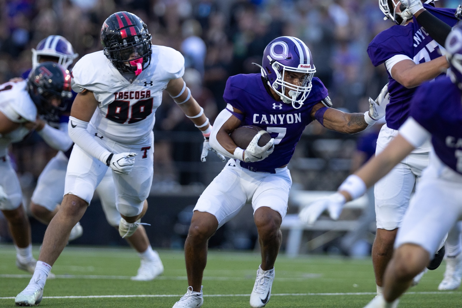THS-CHS-FB-23 | Press Pass Sports Canyon player in purple jersey runs with the ball as a Tasosa defender in white pursues in a college football game.