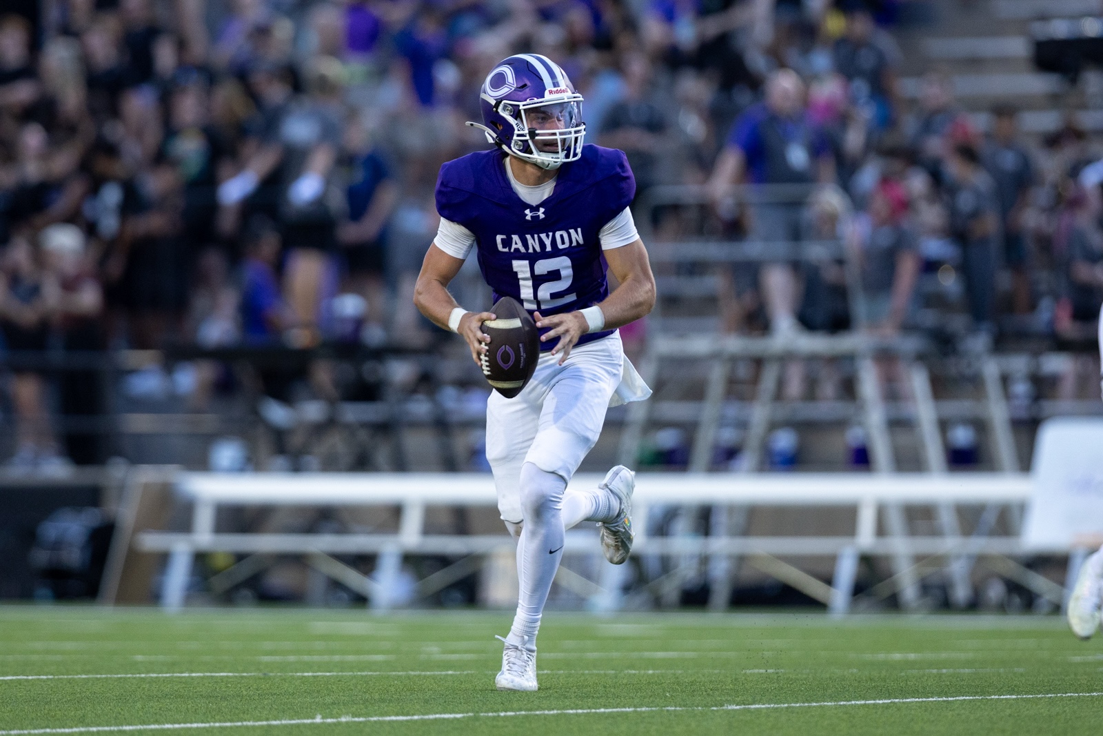 THS-CHS-FB-25 | Press Pass Sports Canyon quarterback in a purple jersey (#12) sprints with the football during a game, crowd in the stands behind him.