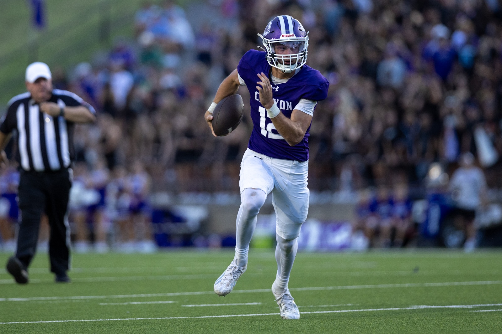 THS-CHS-FB-26 | Press Pass Sports Quarterback in a purple jersey running with the football on a green field, crowd in the stands behind him.