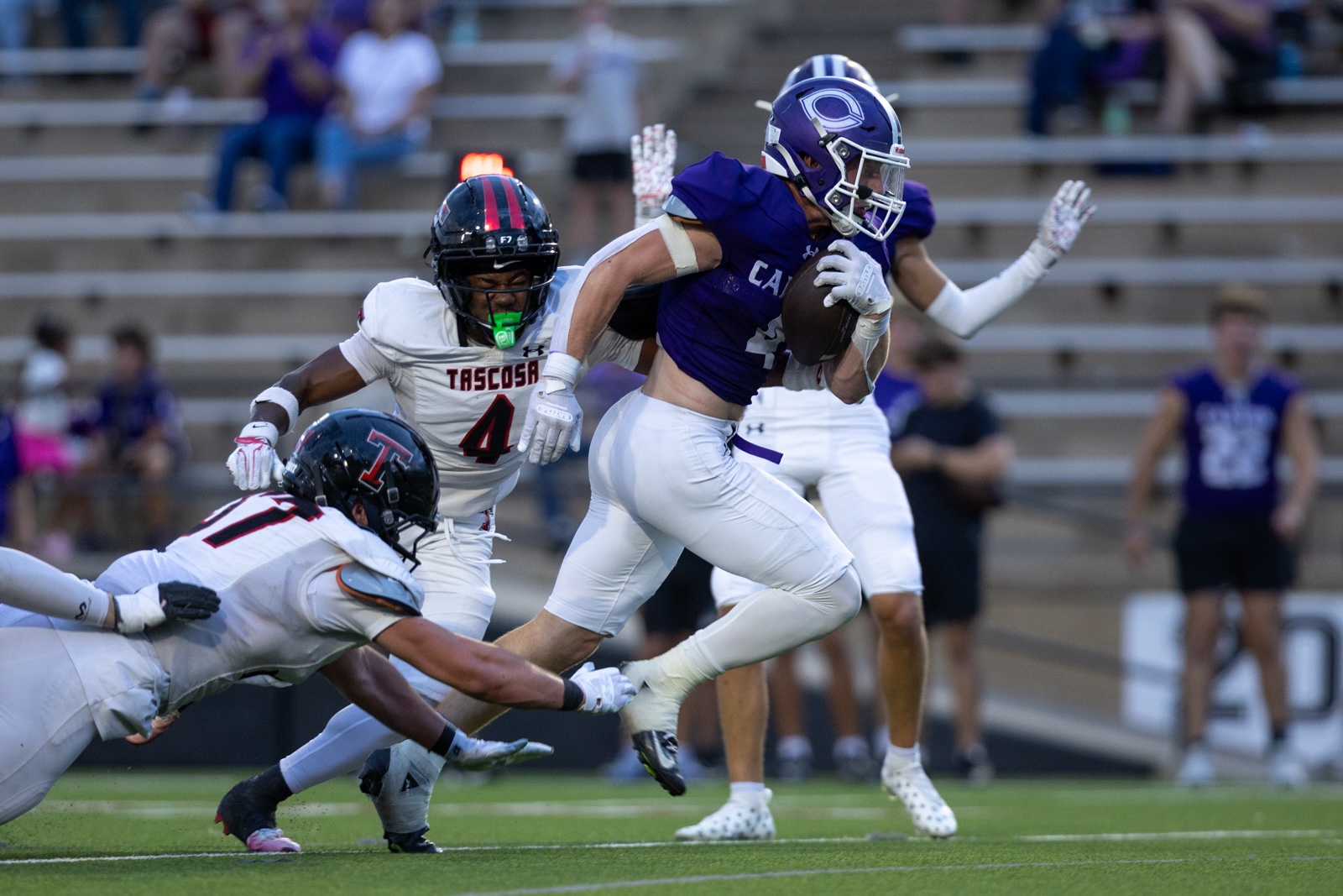 THS-CHS-FB-27 | Press Pass Sports Purple football player carries ball while sprinting past white-jersey defenders on a green field.