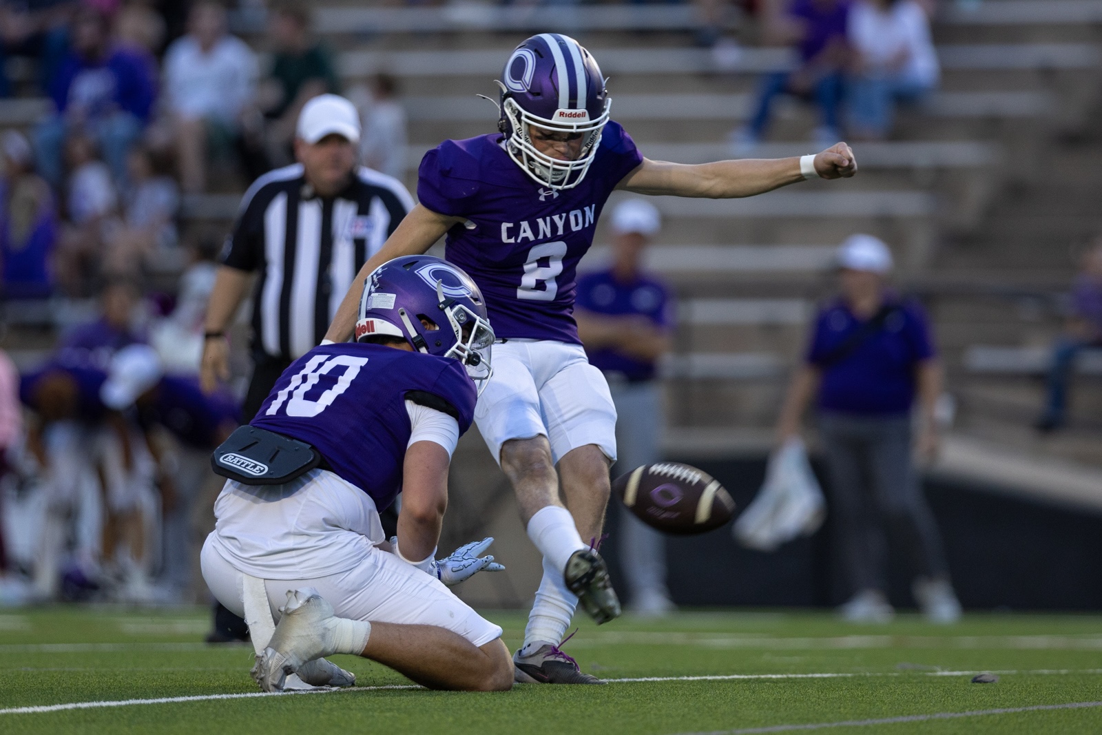 THS-CHS-FB-29 | Press Pass Sports Two Canyon players in purple uniforms collide on a football field as one leaps to kick the ball midair.