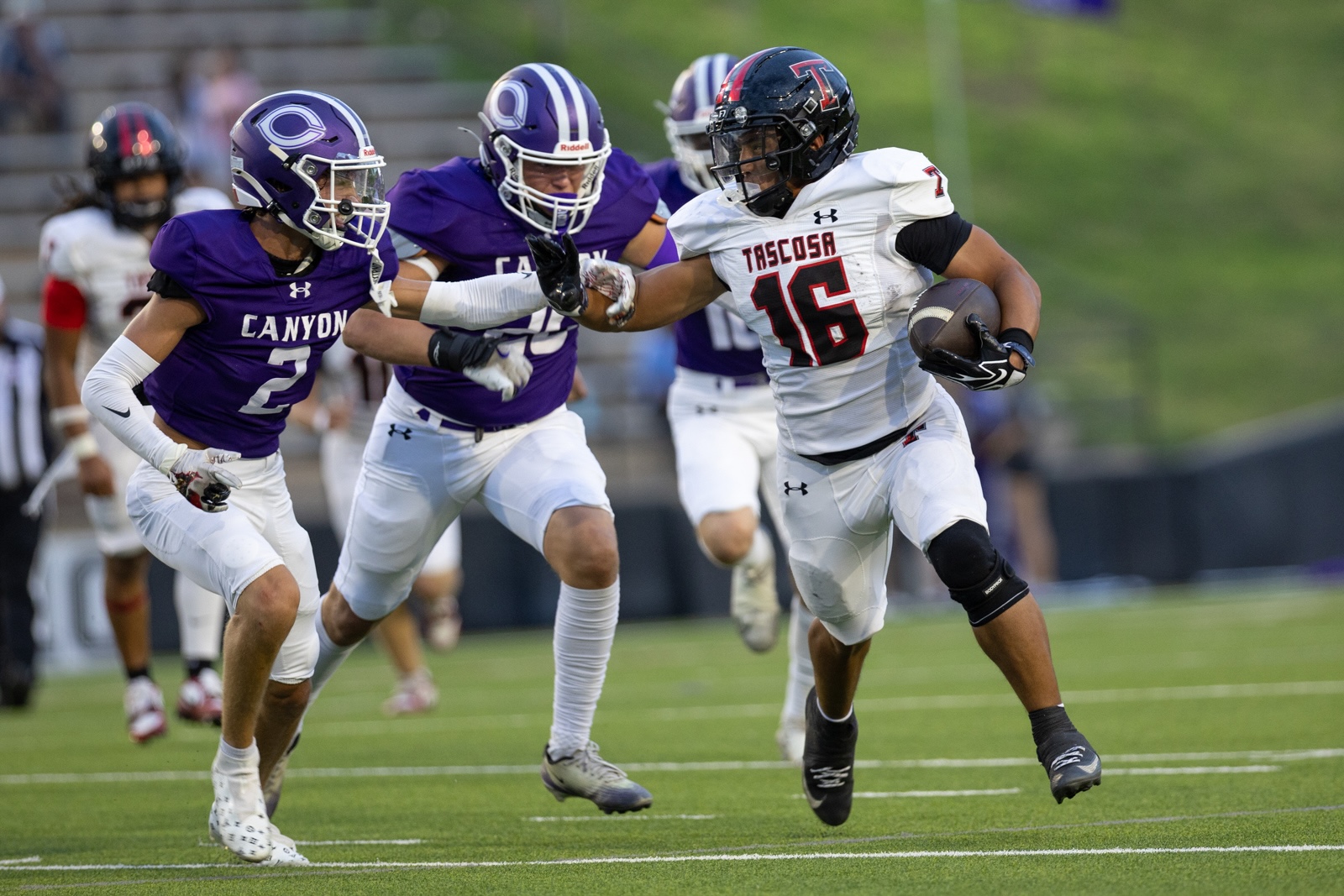 THS-CHS-FB-31 | Press Pass Sports Tascosa #16 runs with the football as two Canyon defenders in purple close in on him on a green field.