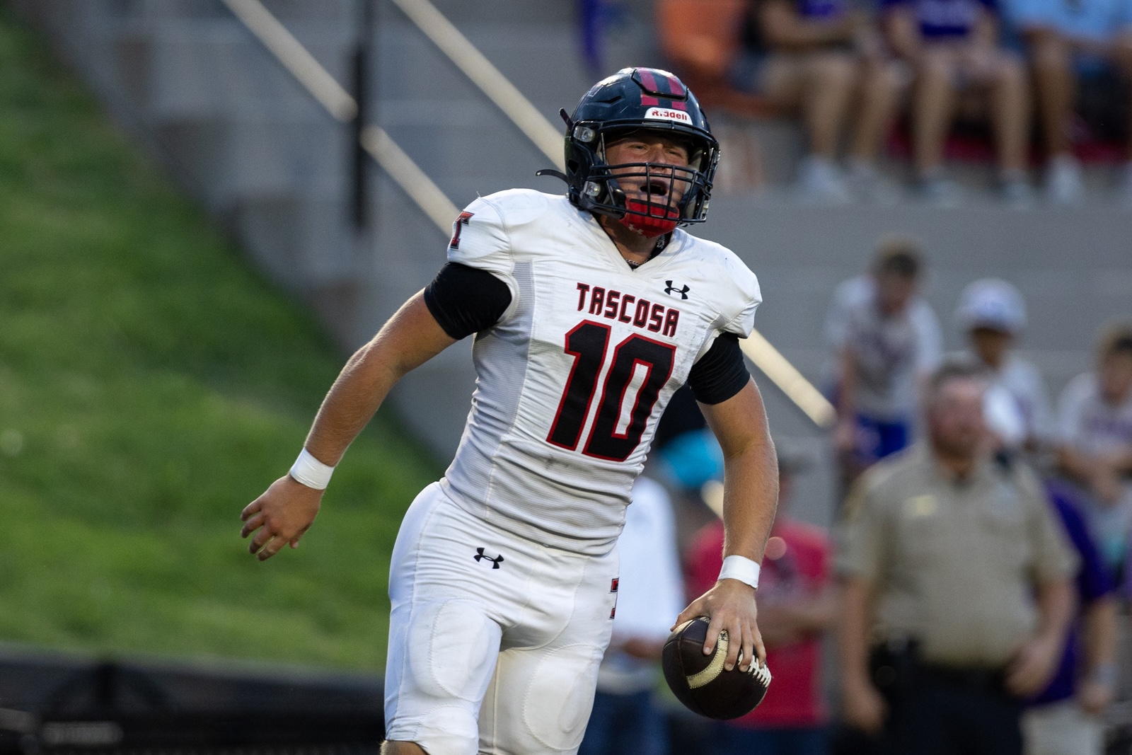 THS-CHS-FB-32 | Press Pass Sports Tascosa football player wearing number 10 in a white uniform runs with the ball during a game, wearing a dark helmet and pads with a crowd in the background