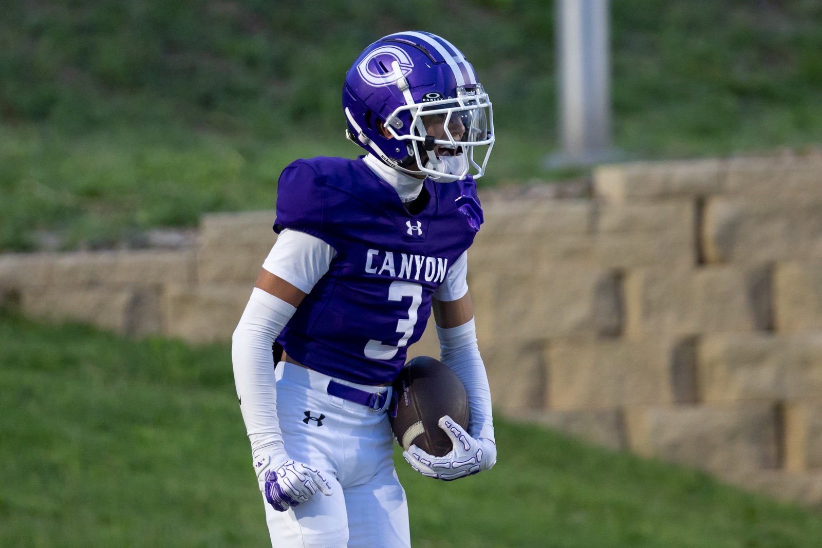 THS-CHS-FB-34 | Press Pass Sports Canyon football player wearing purple jersey #3 and white pants holds a football on a grassy field.