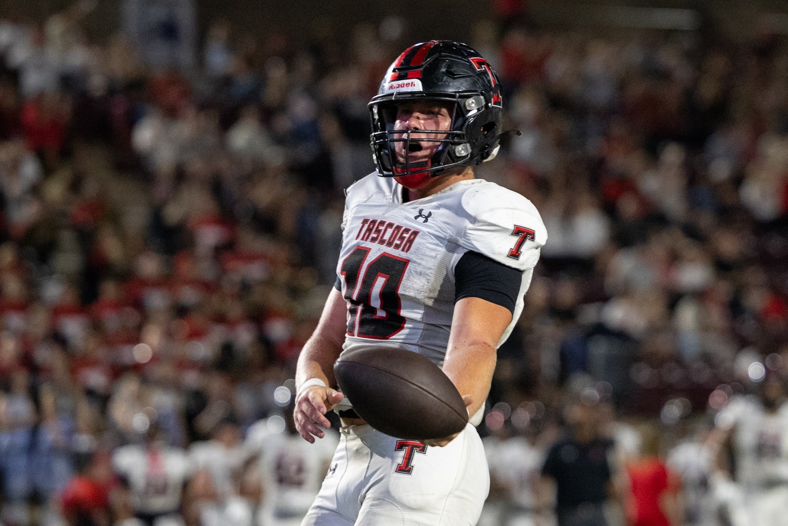 THS-CHS-FB-39 | Press Pass Sports Football player in white uniform with number 10, holding a football mid-air during a game with a crowded stadium in the background