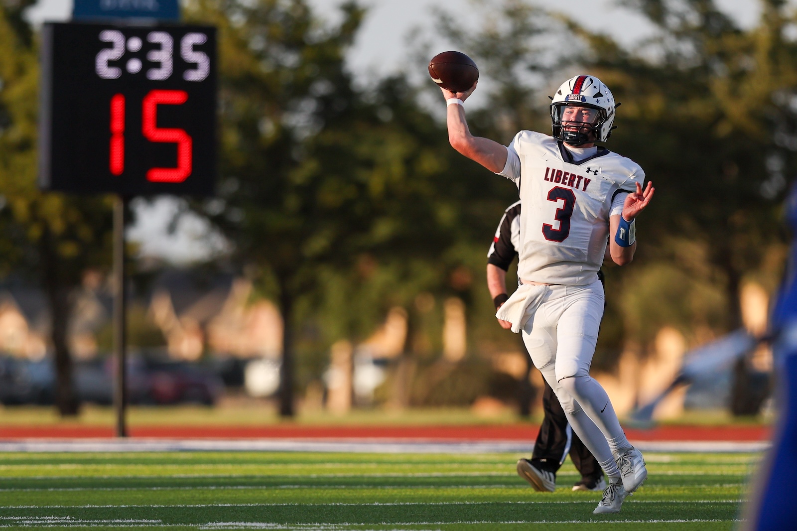 Seabolt Chase-16858 | Press Pass Sports Liberty University quarterback in a white jersey number 3 throwing a pass on a green field, scoreboard in the background showing 2:35 and 15.