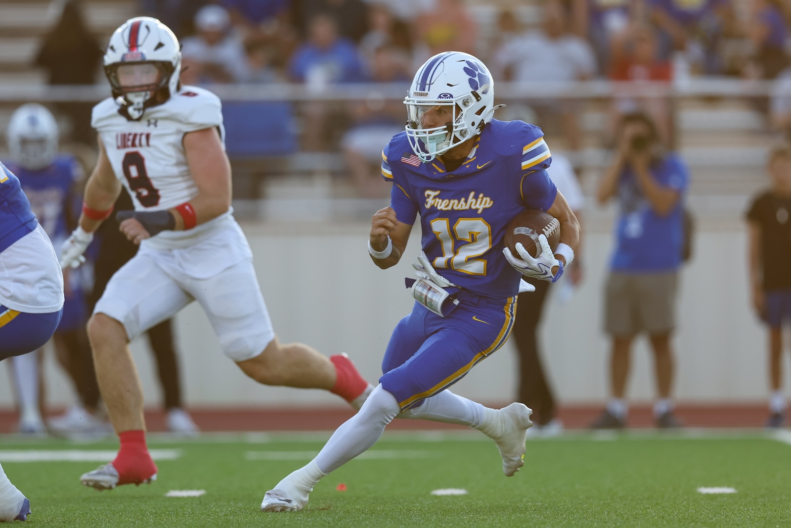 Seabolt Chase-17308 | Press Pass Sports Blue and yellow football player wearing number 12 runs with the ball down the field, pursued by opponents.