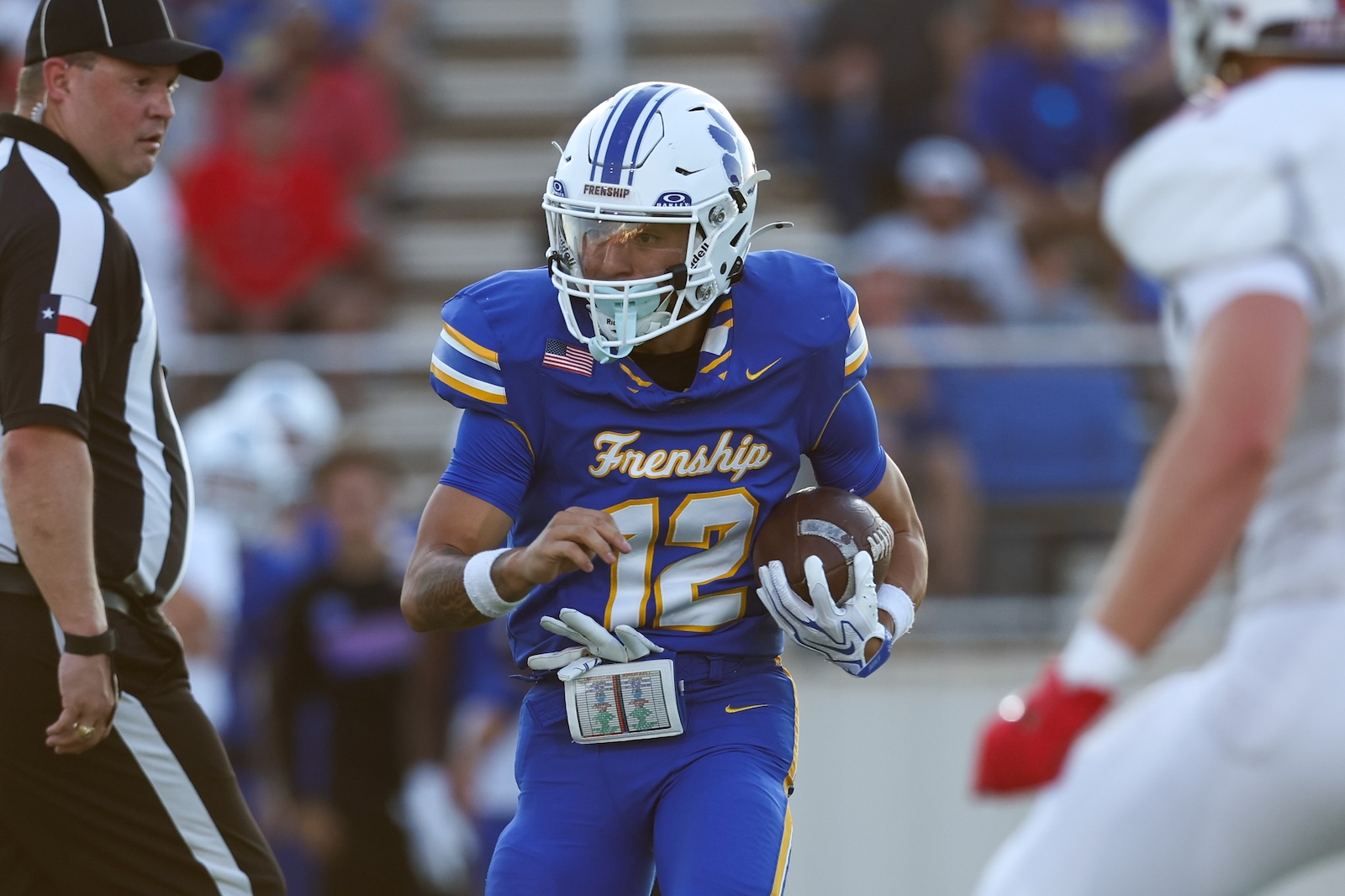 Seabolt Chase-17320 | Press Pass Sports American football player in a blue Frenship uniform (number 12) runs with the ball during a game, with a referee nearby.