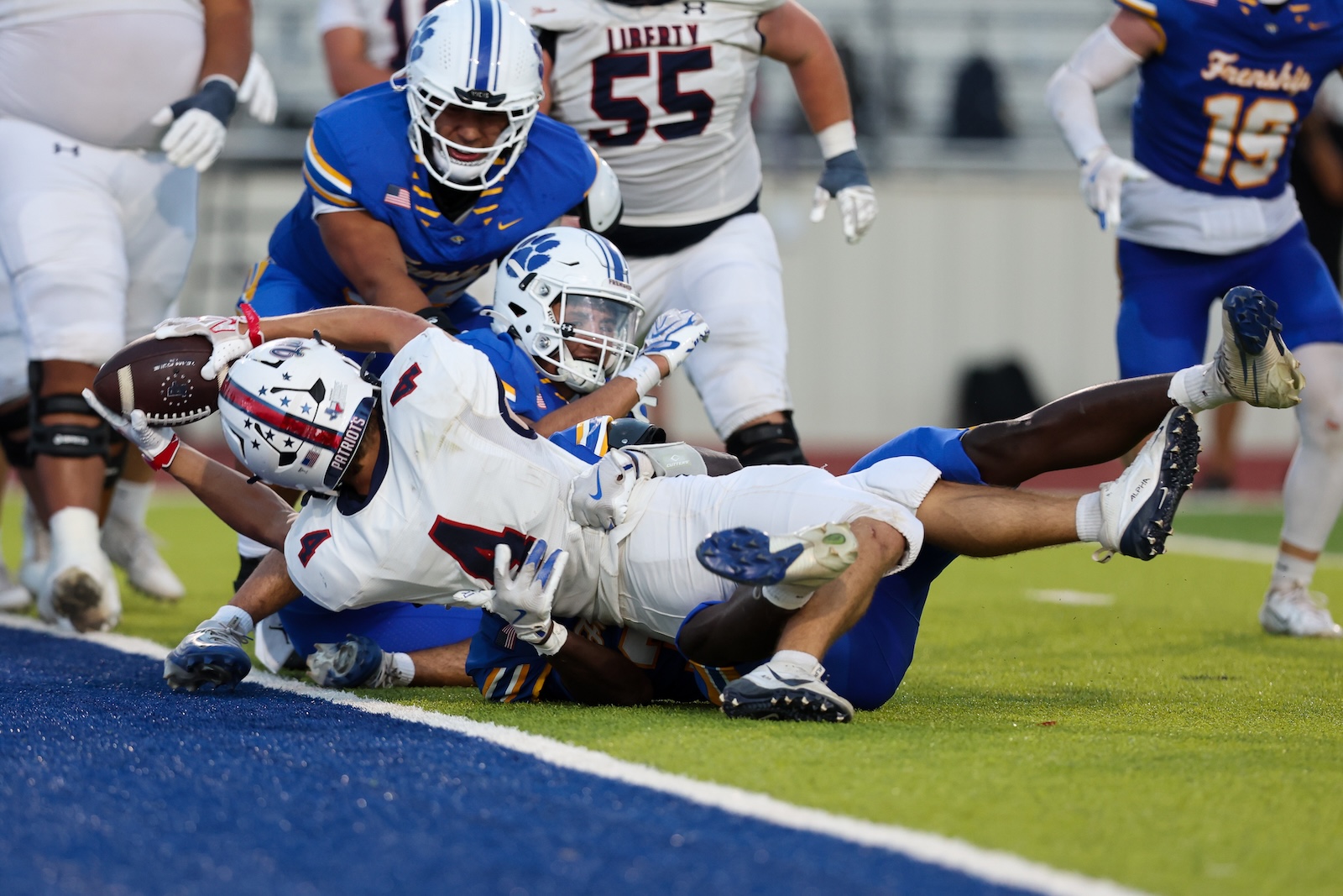 Seabolt Chase-17864 | Press Pass Sports Football players pile up near the end zone line as a white-uniformed runner is tackled by a blue-uniformed defender during a tackle on the grass field.
